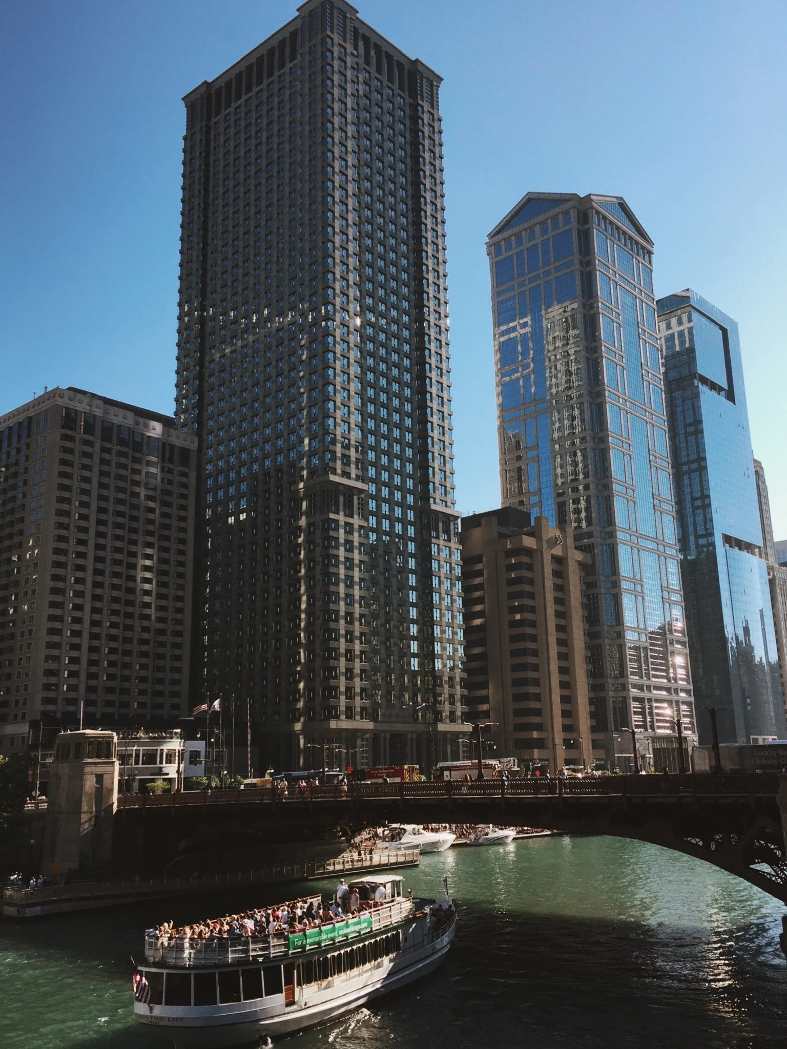Skyscrapers and modern buildings along a river with a boat carrying passengers in the foreground.