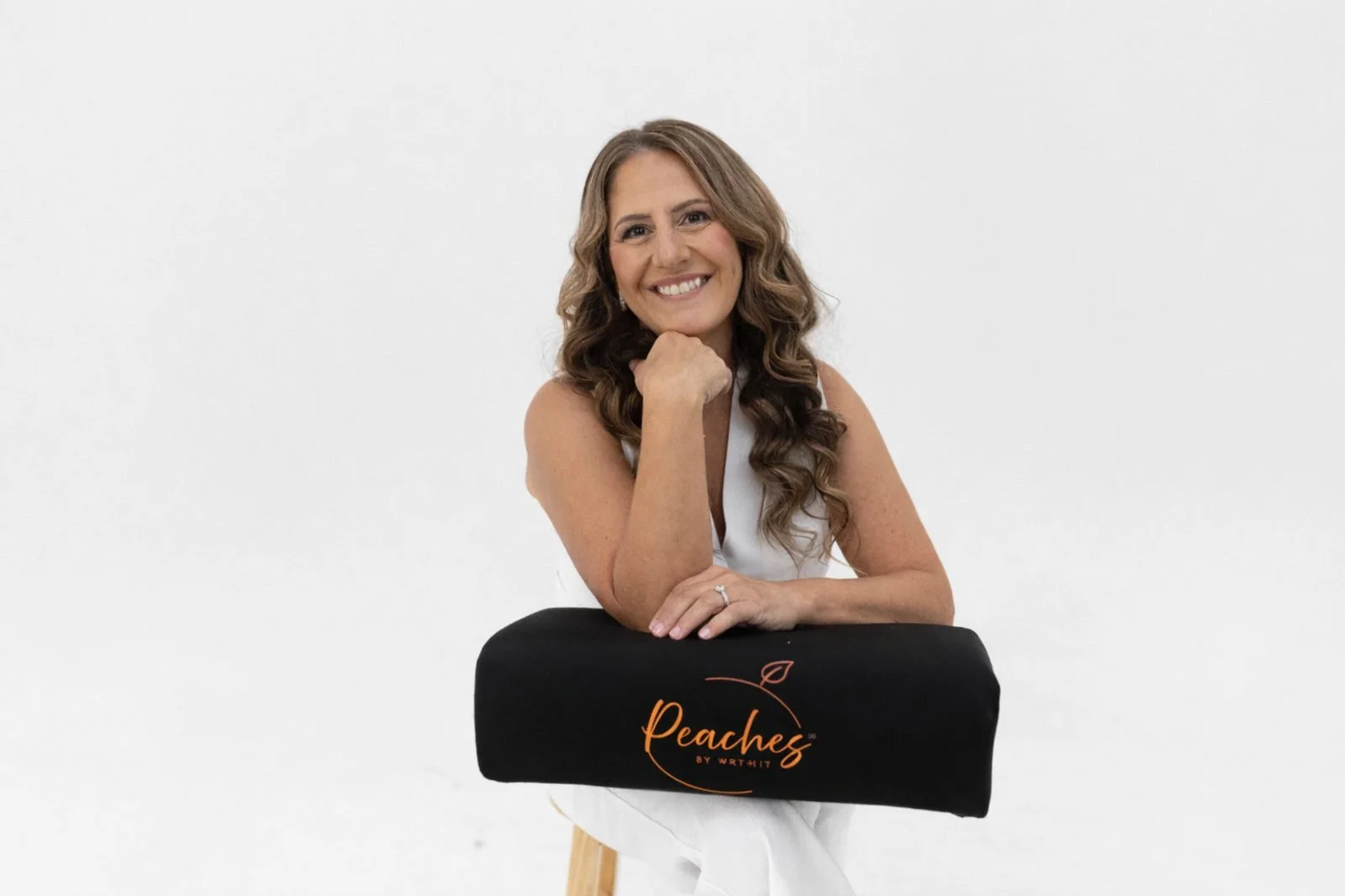 Monica Skalsky, Founder of Wrthit, wearing a white vest and pants with her elbow on The Bellini BBL Pillow