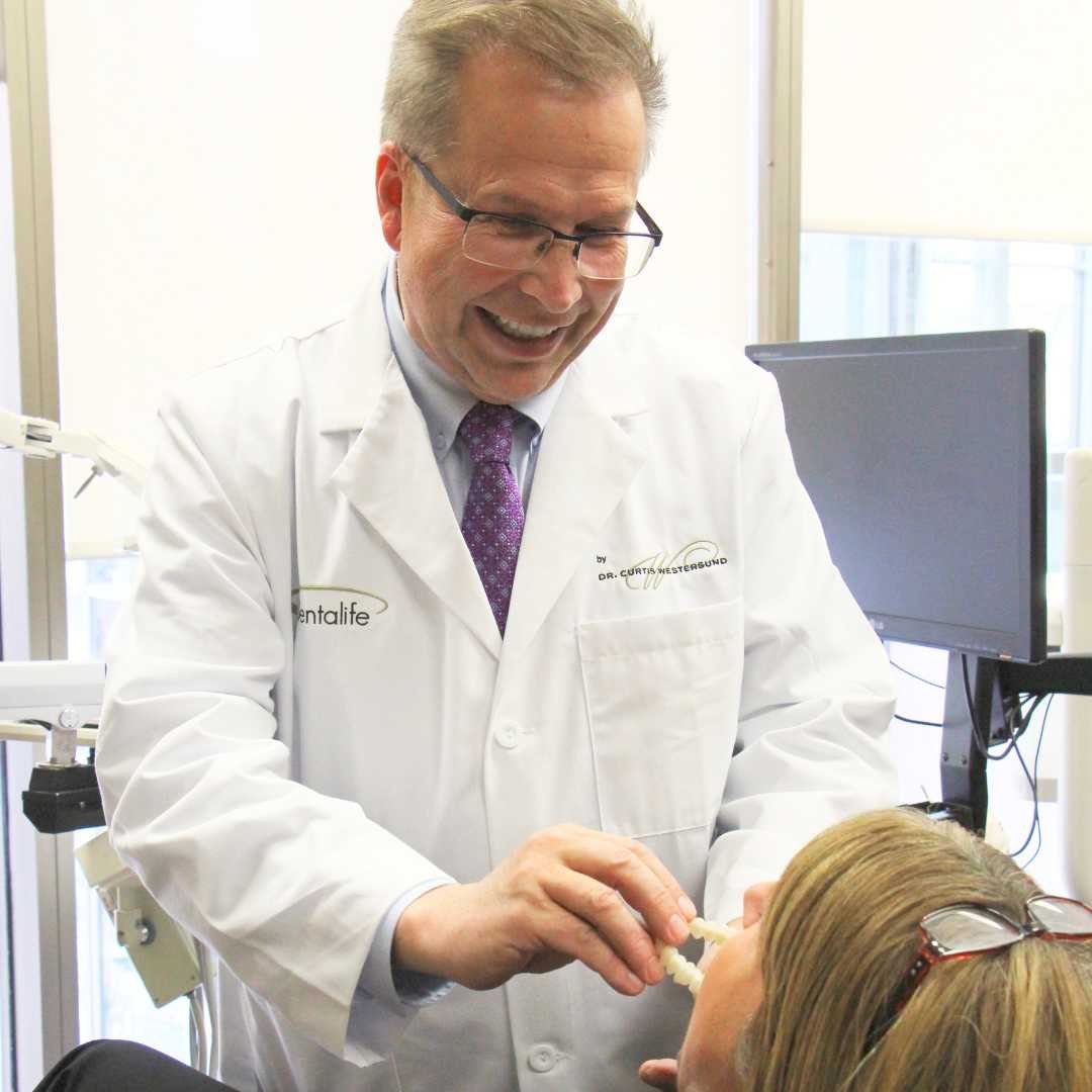 A male dentist in a white coat demonstrates a dental tool to a female patient in a dental clinic.
