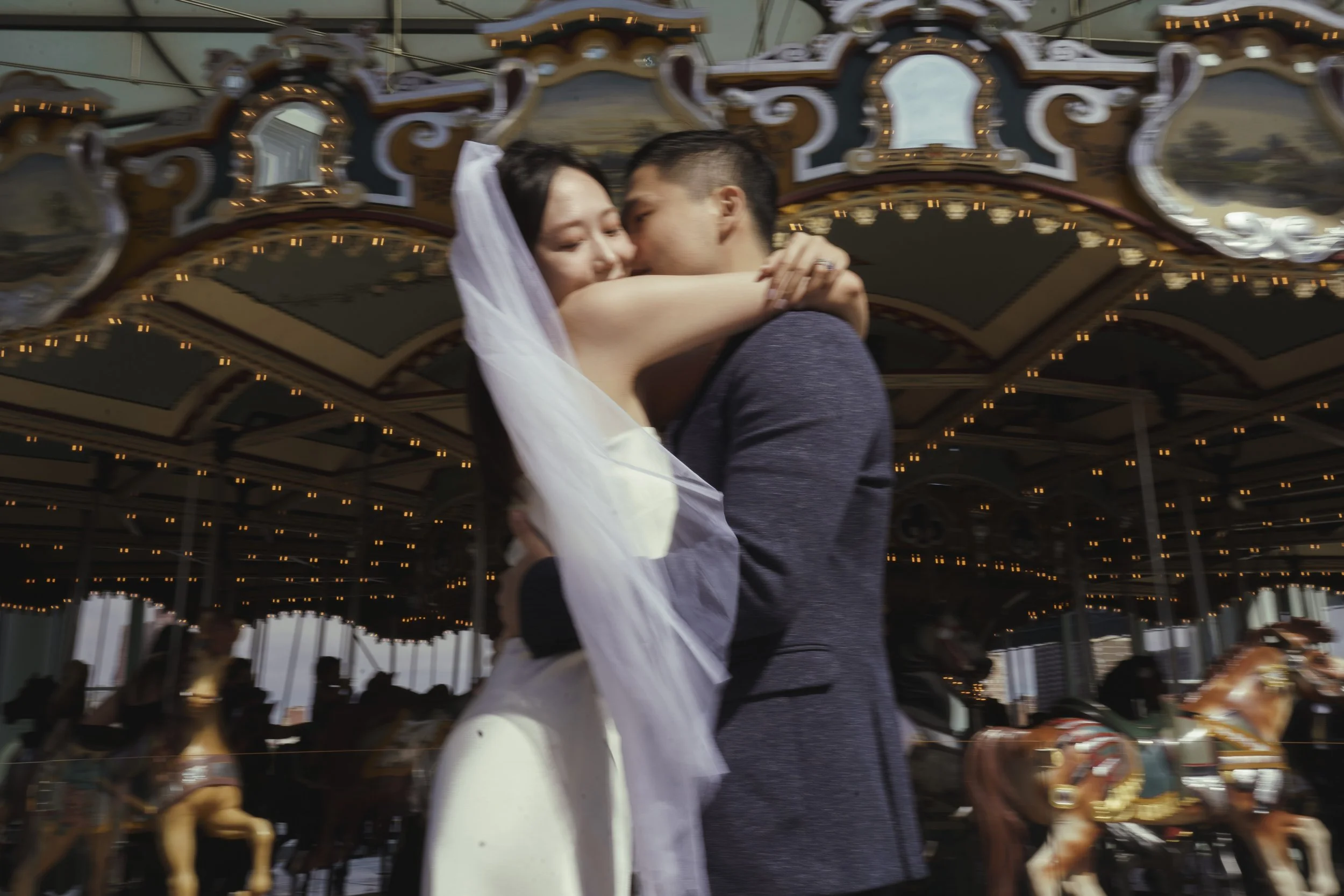 A couple dancing closely in front of a carousel with ornate decorations and lights.