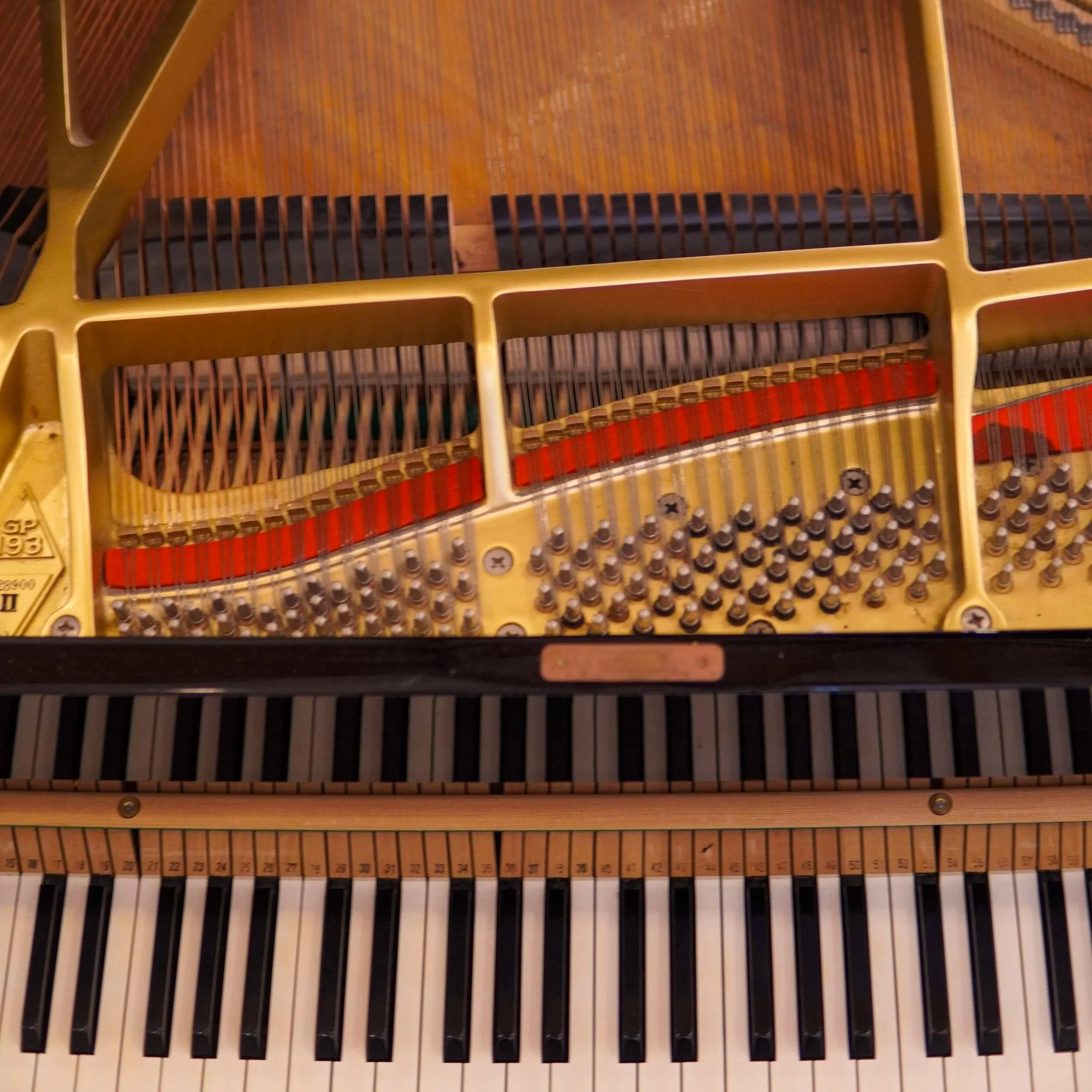 Disassembled piano with its frame, strings, and various wooden and metal components scattered on a red surface.