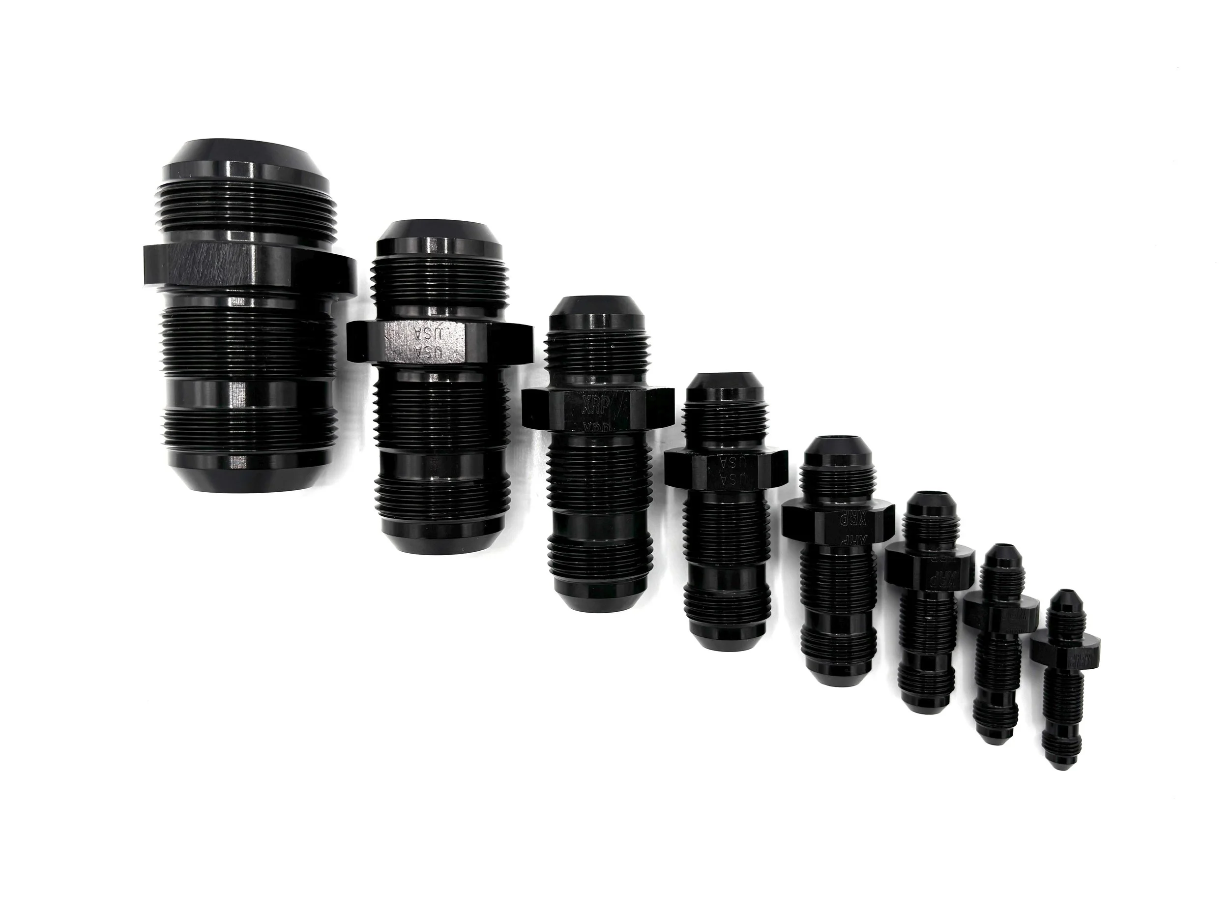 XRP straight bulkhead union fitting. Black in color. Various sizes from largest to smallest, left to right.