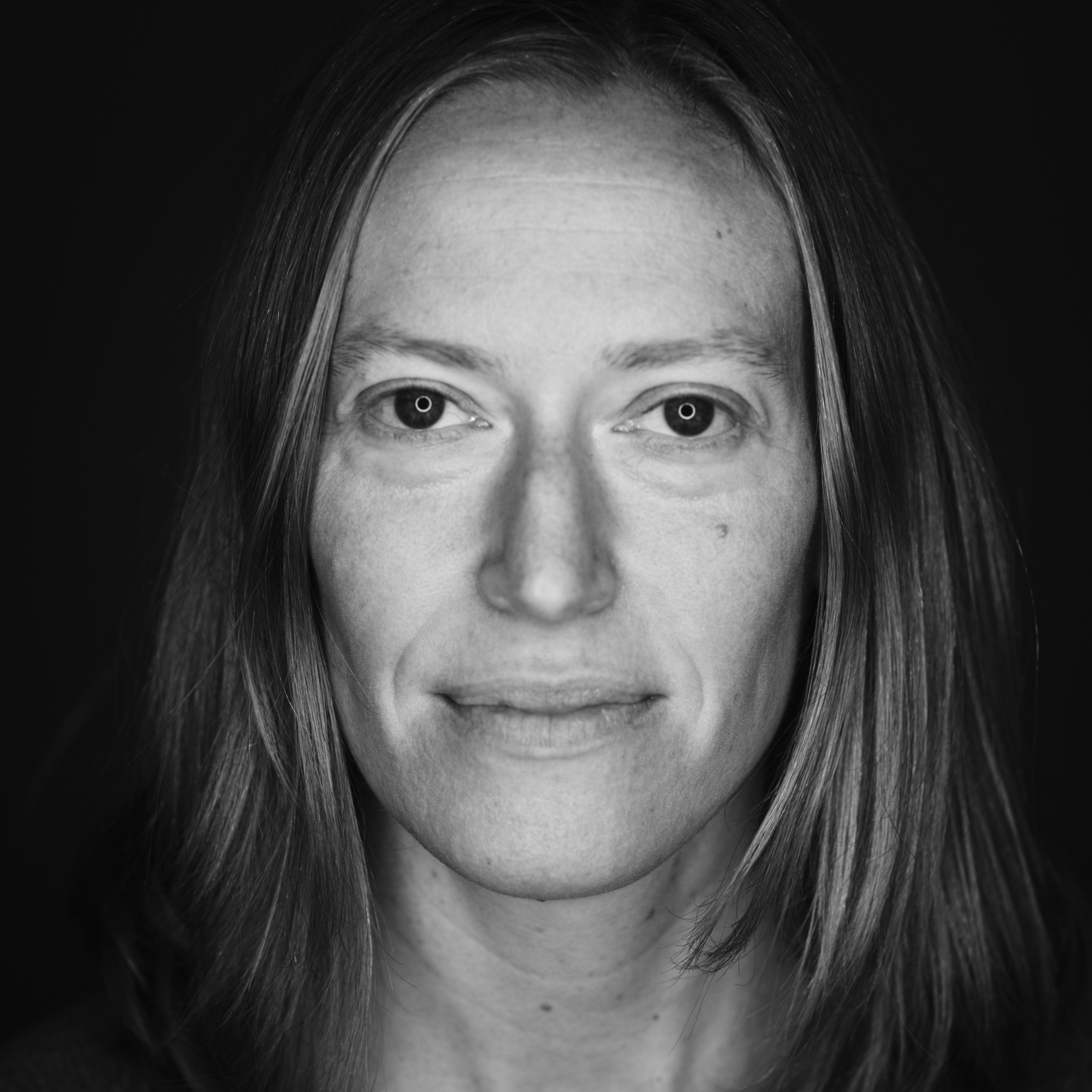 Close-up black and white portrait of a woman's face with long hair, looking directly at the camera.