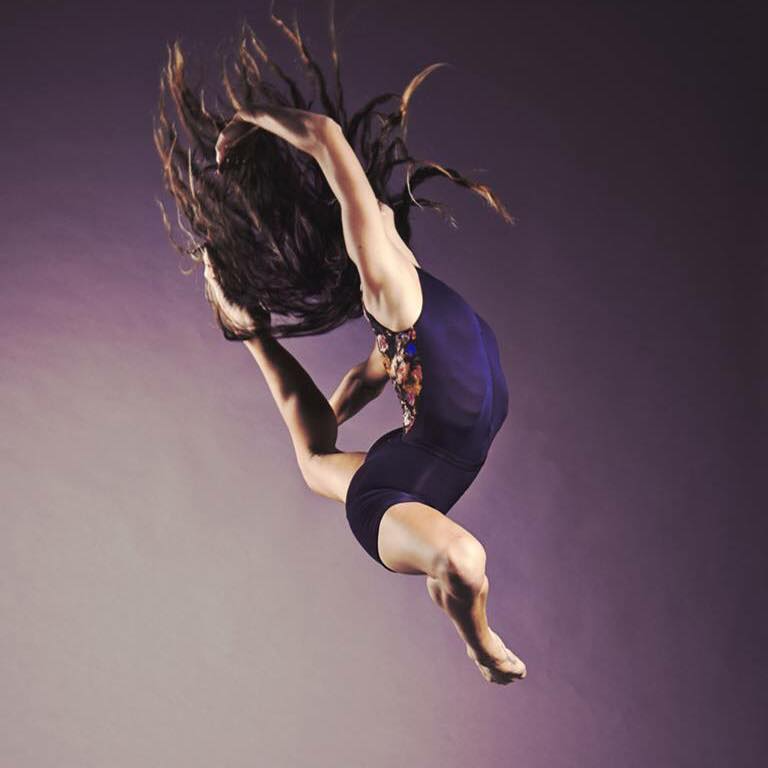 A woman performing an acrobatic flip mid-air against a neutral background.