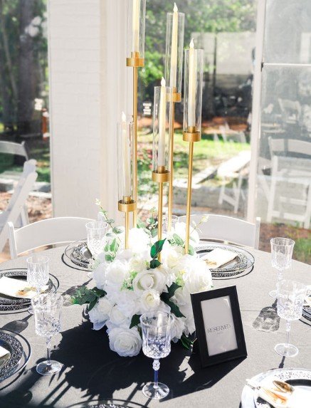 Elegant table centerpiece with white flowers and tall gold candle holders on a dining table set for a formal event.