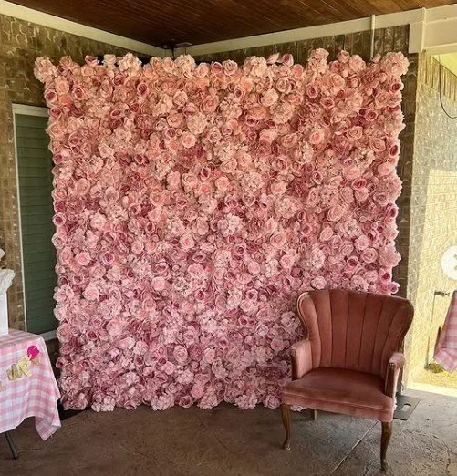 A decorative backdrop made of pink roses with a brown vintage armchair in front of it.