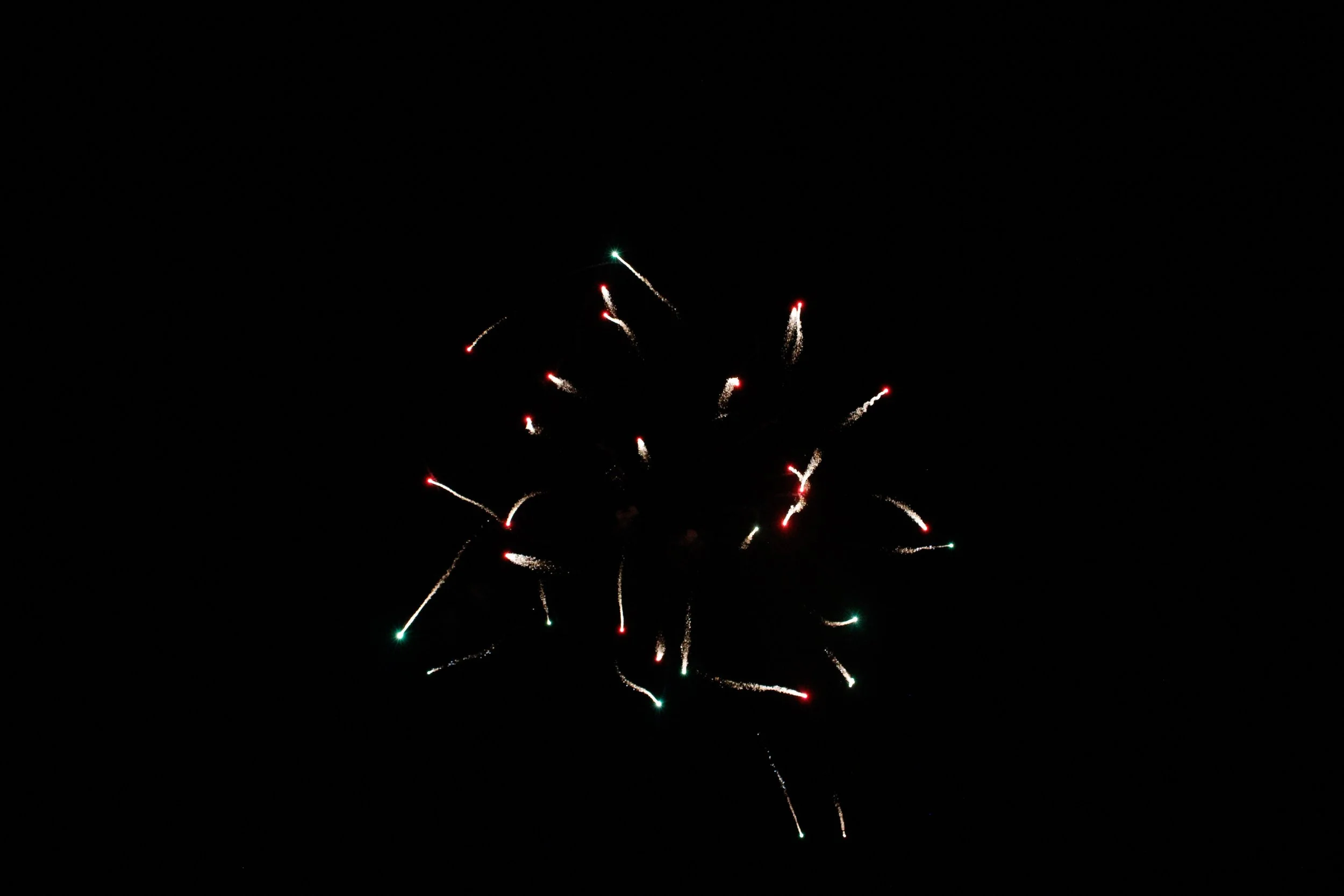 Fireworks exploding in a dark night sky with streaks of red, green, and white lights.