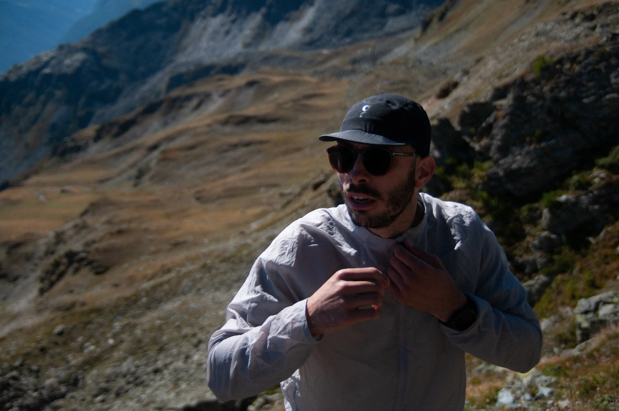 Trail runner in a light jacket and cap on a sunlit alpine mountainside, outdoor adventure photography