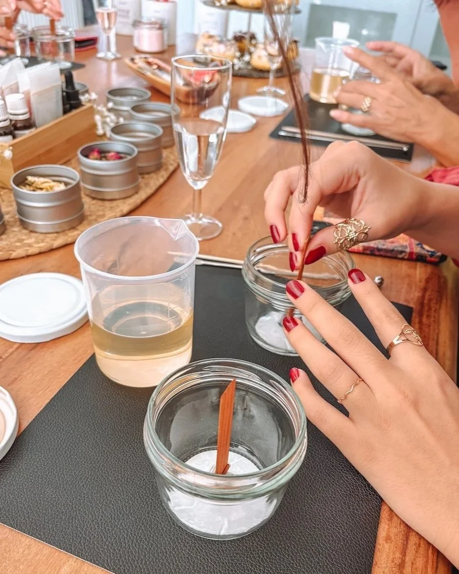 Personen bei Kerzenworkshop mit verschiedenen Gläsern, Wachs, Duftstoffen und Deko auf einem Holztisch.