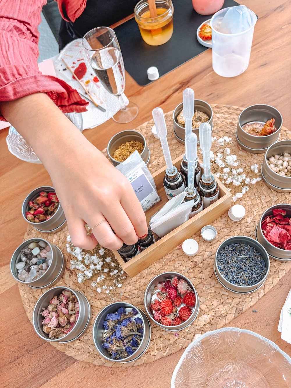 Ein Tisch mit verschiedenen Duftölen, Pipetten,  einer Holzschale und kleinen Dosen mit getrockneten Blüten.