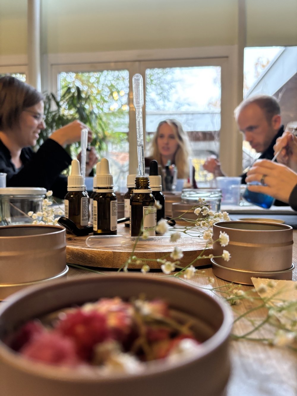 Menschen bei Kerzenworkshop mit Duftflaschen und Deko auf einem Tisch, im Hintergrund ein Fenster mit Ausblick nach draußen.