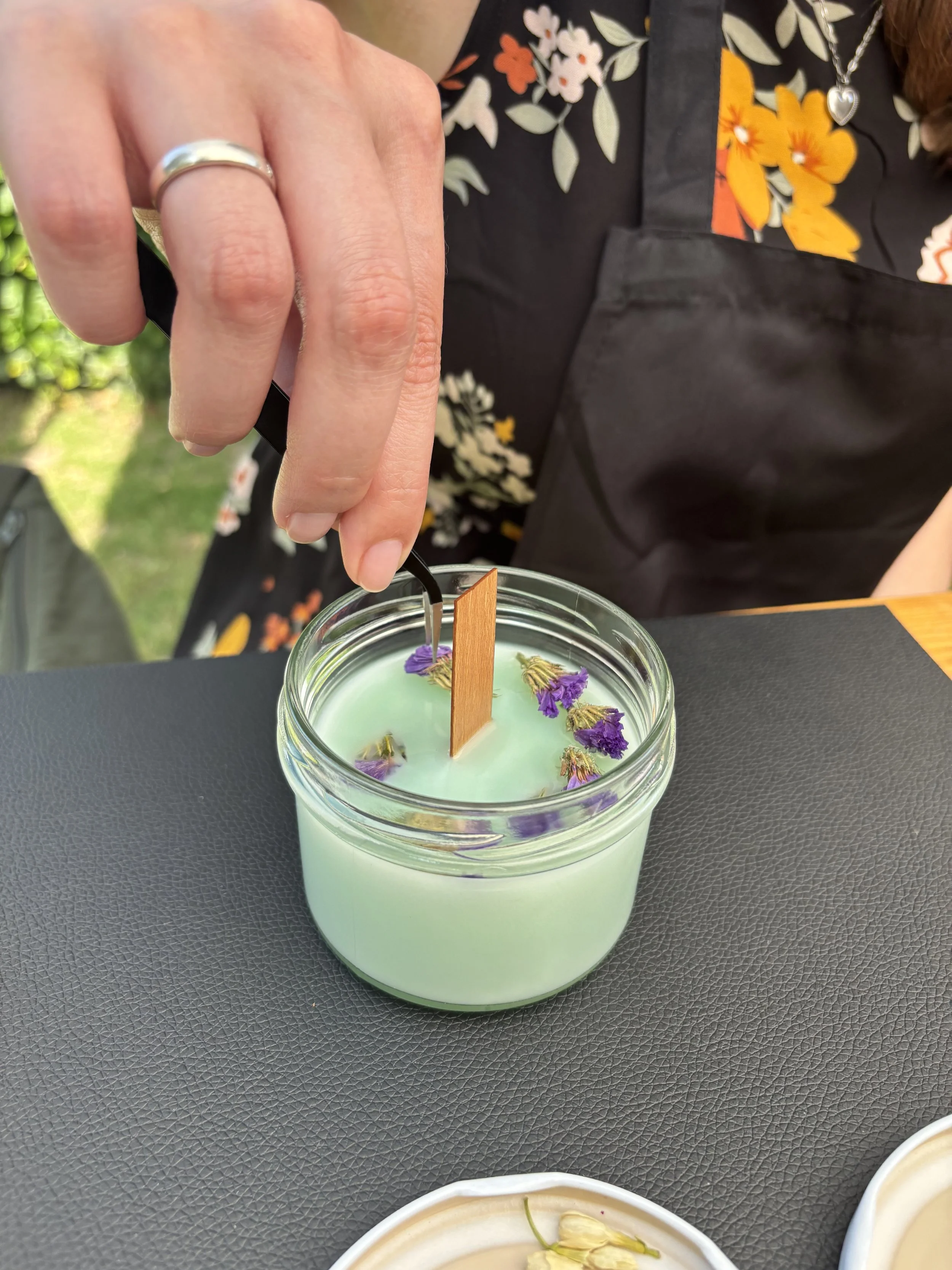 Eine Hand zieht einen Docht in einem Kerzenglas ein.