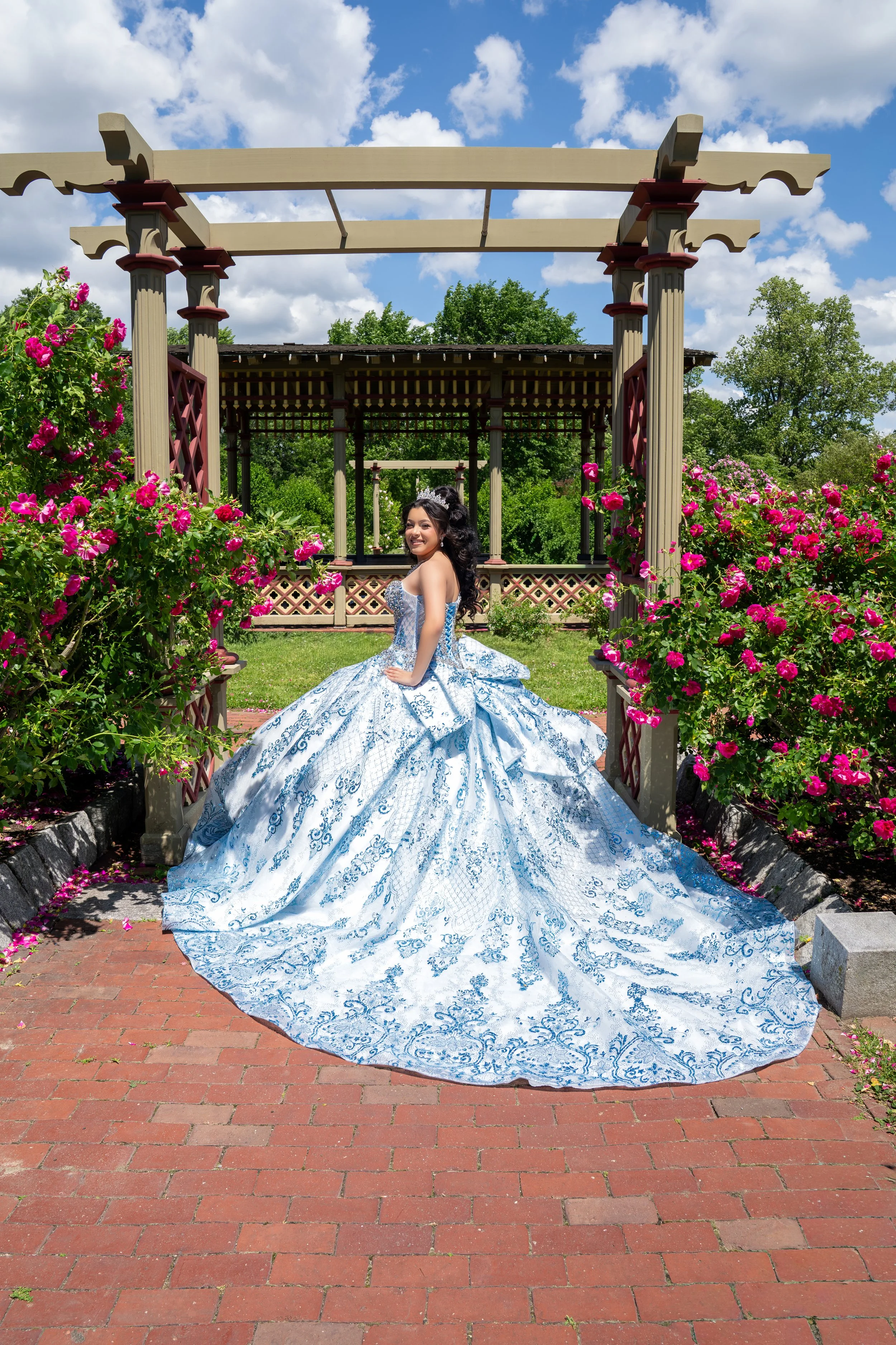 A bride and groom on their wedding day outdoors during autumn, with colorful fall trees in the background. The bride is wearing a white lace wedding dress and holding a bouquet of roses, while the groom is dressed in a dark suit, and they are embracing affectionately.