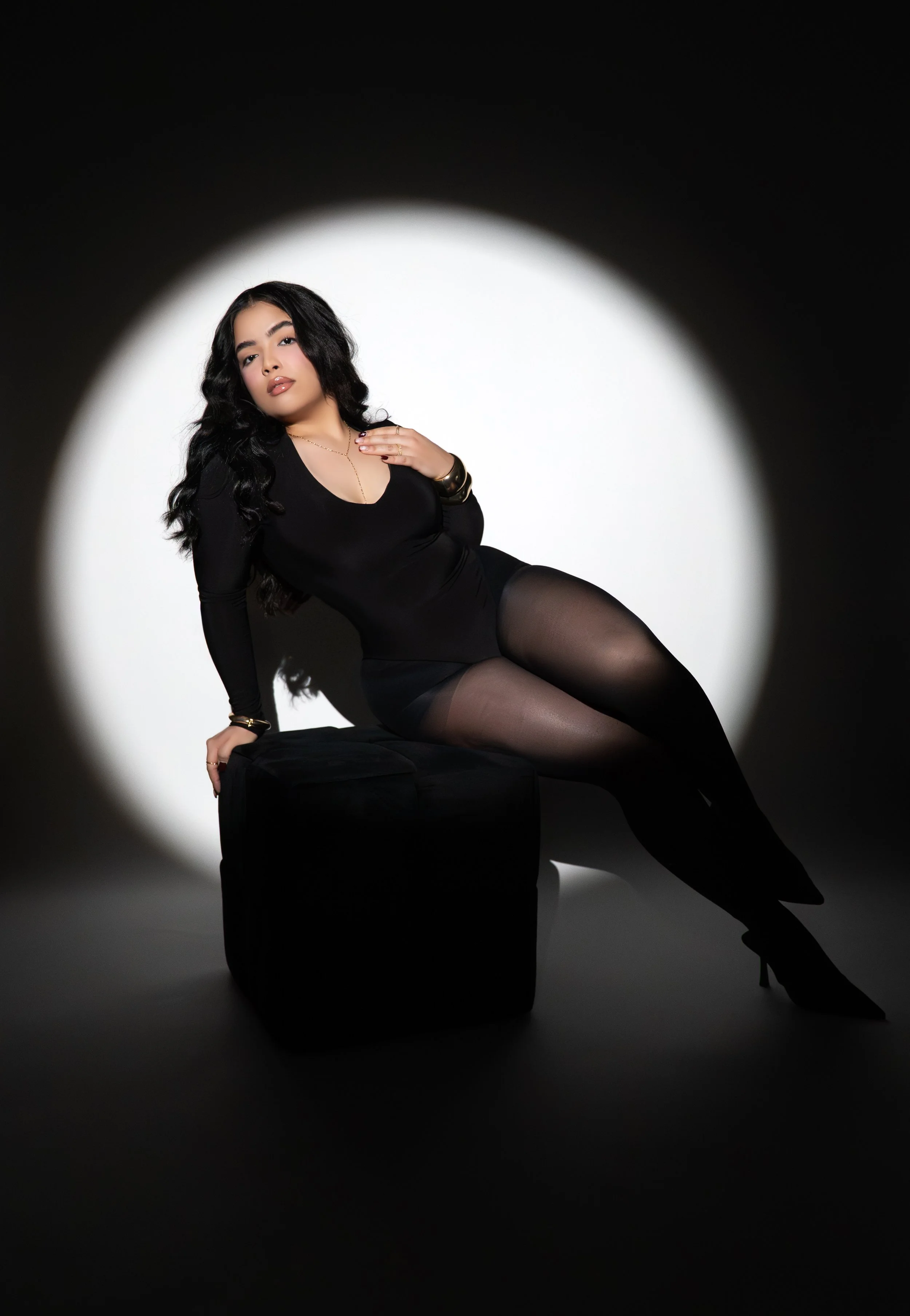 A woman in a black dress, black coat, and high heels walking at night on a city street, smiling and looking down.