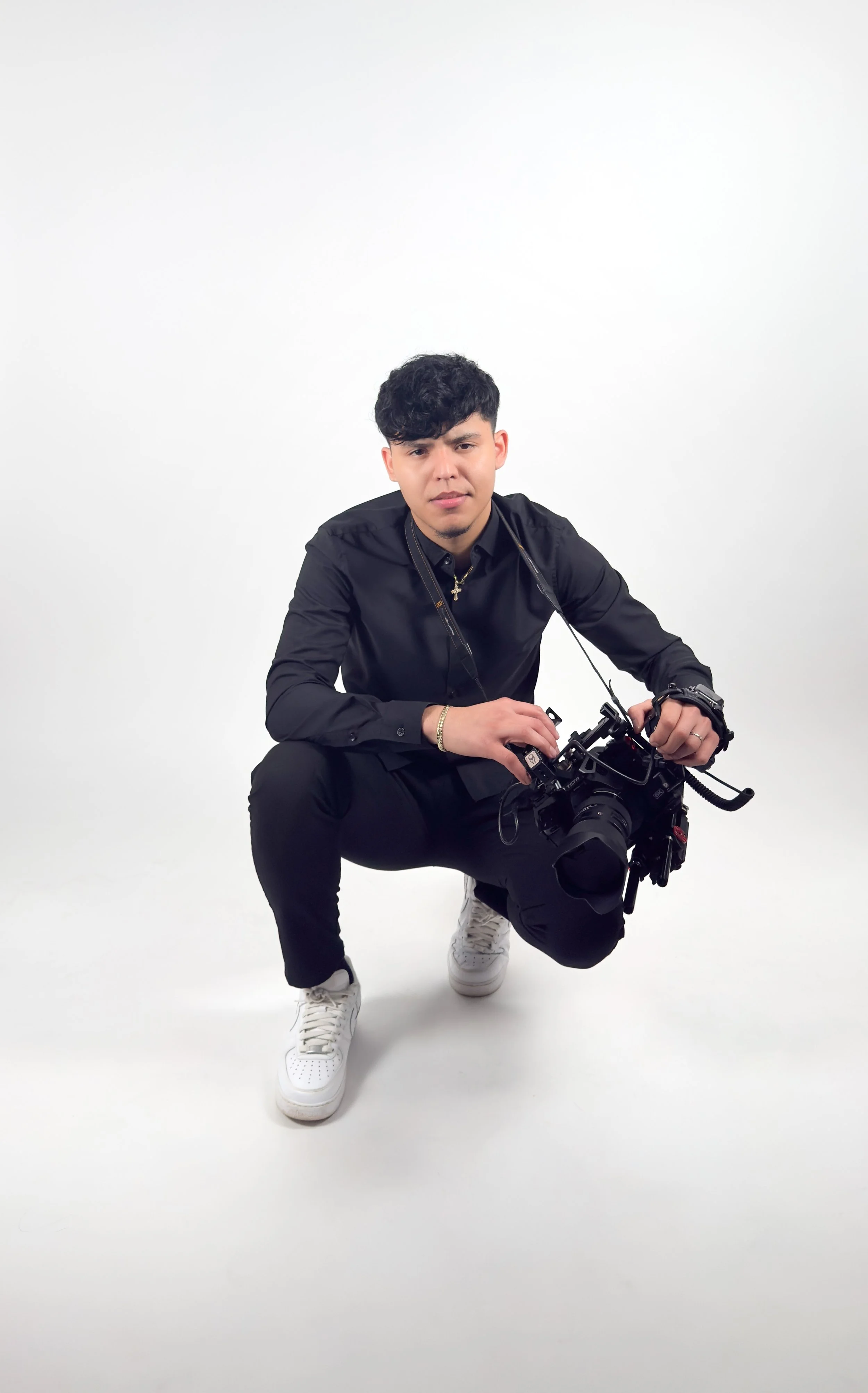 Young man crouching with camera in a studio with white background.