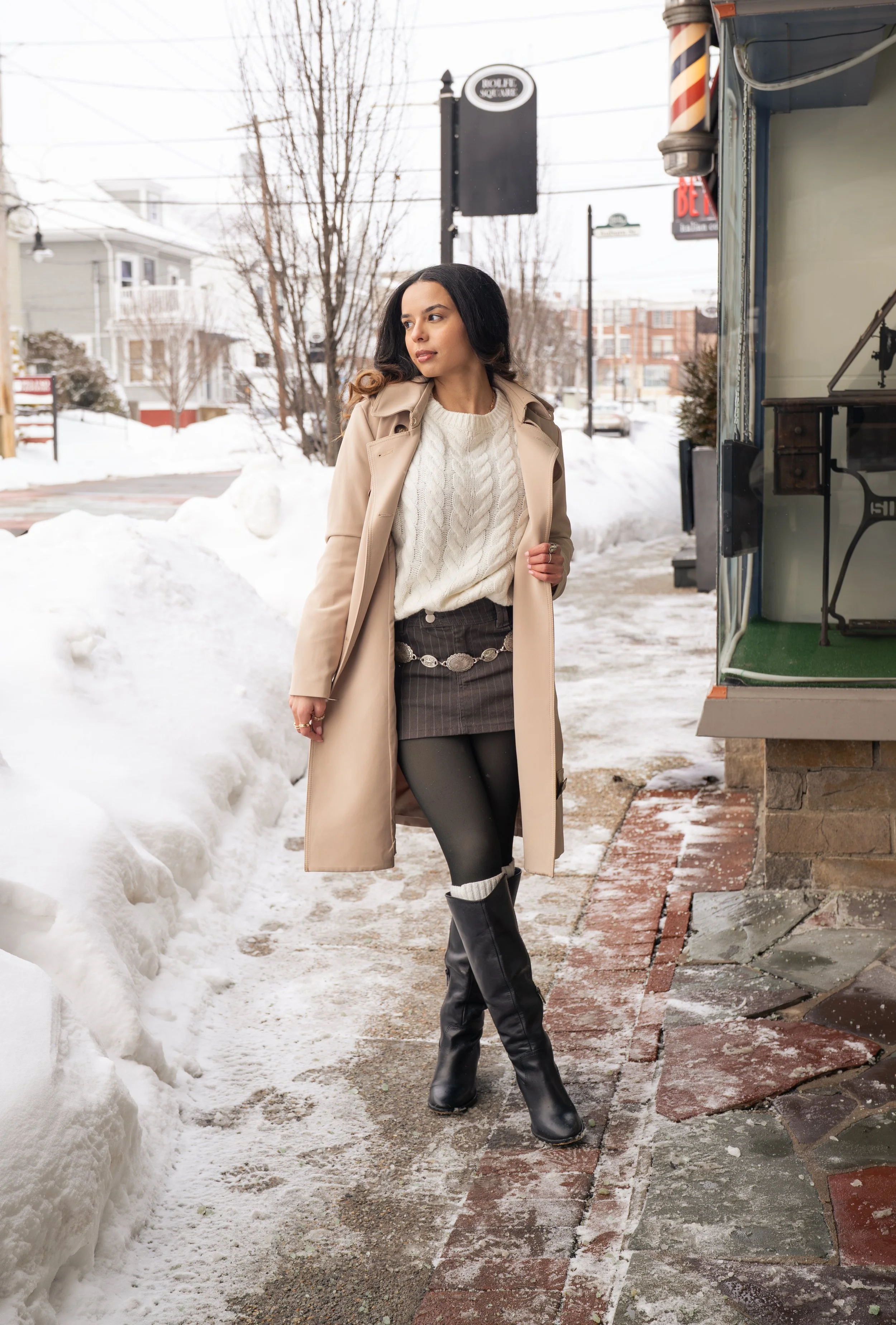 A young woman in a floral dress sitting on the beach with a man holding a bouquet of pink and white roses.