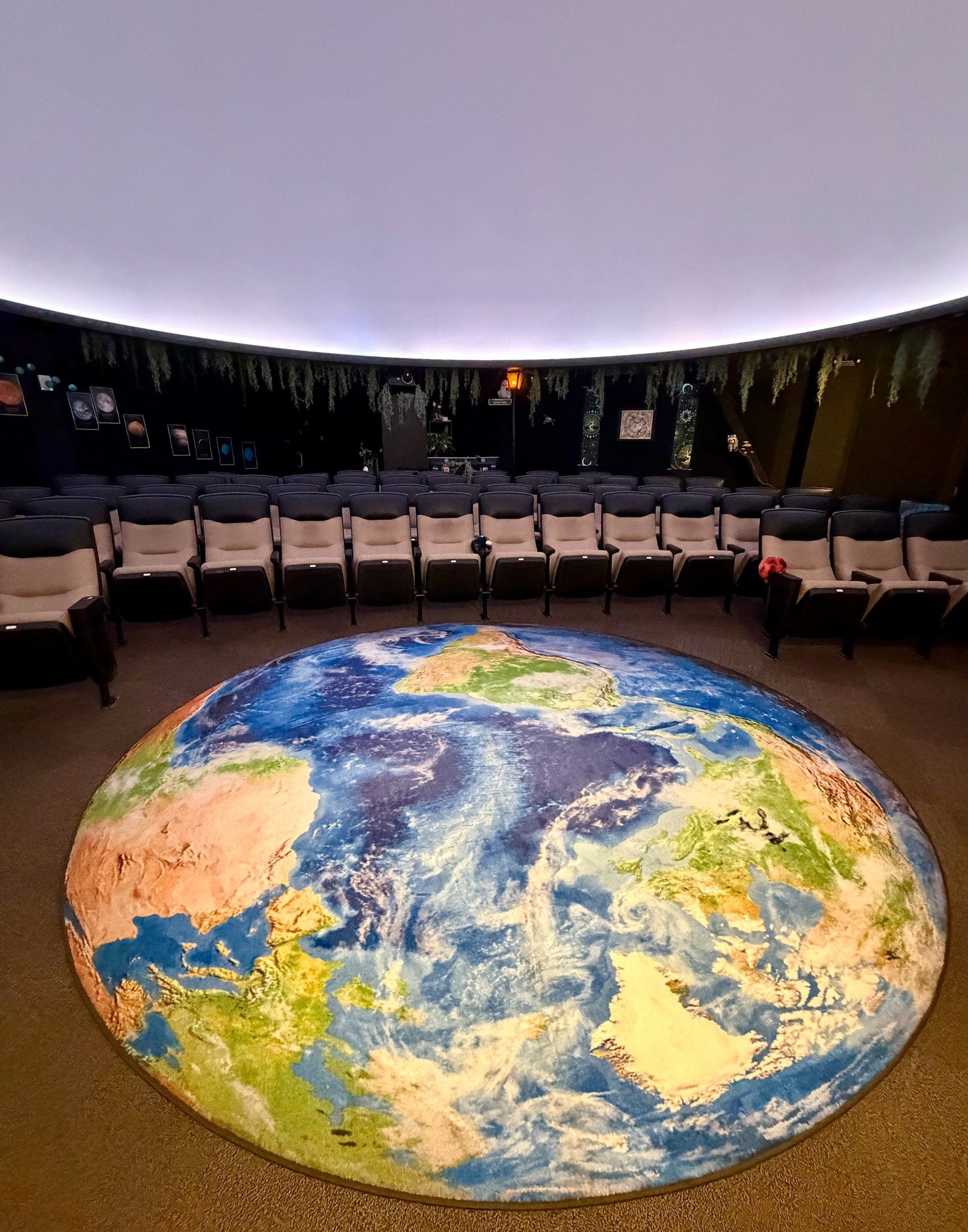 A circular projection of Earth on the floor of a planetarium with rows of theater seats and a domed ceiling.