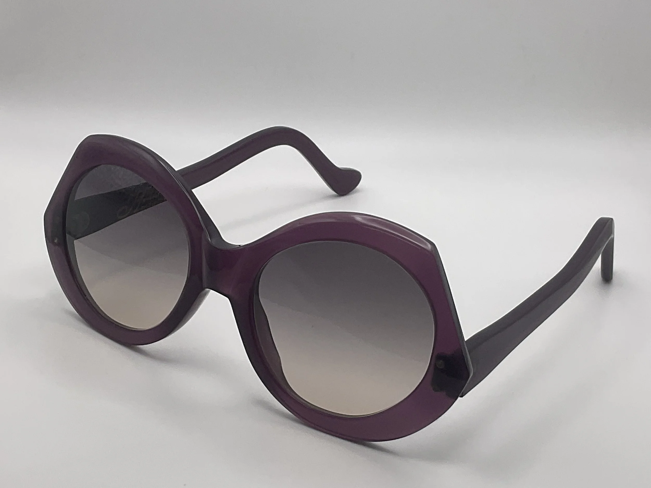 Purple sunglasses with gradient tinted lenses placed on a white surface.