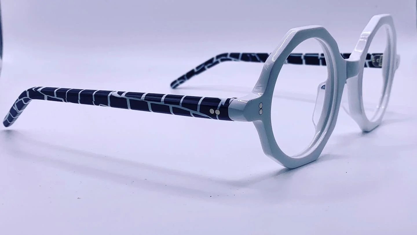 White eyeglasses with black-patterned temples on a white surface.