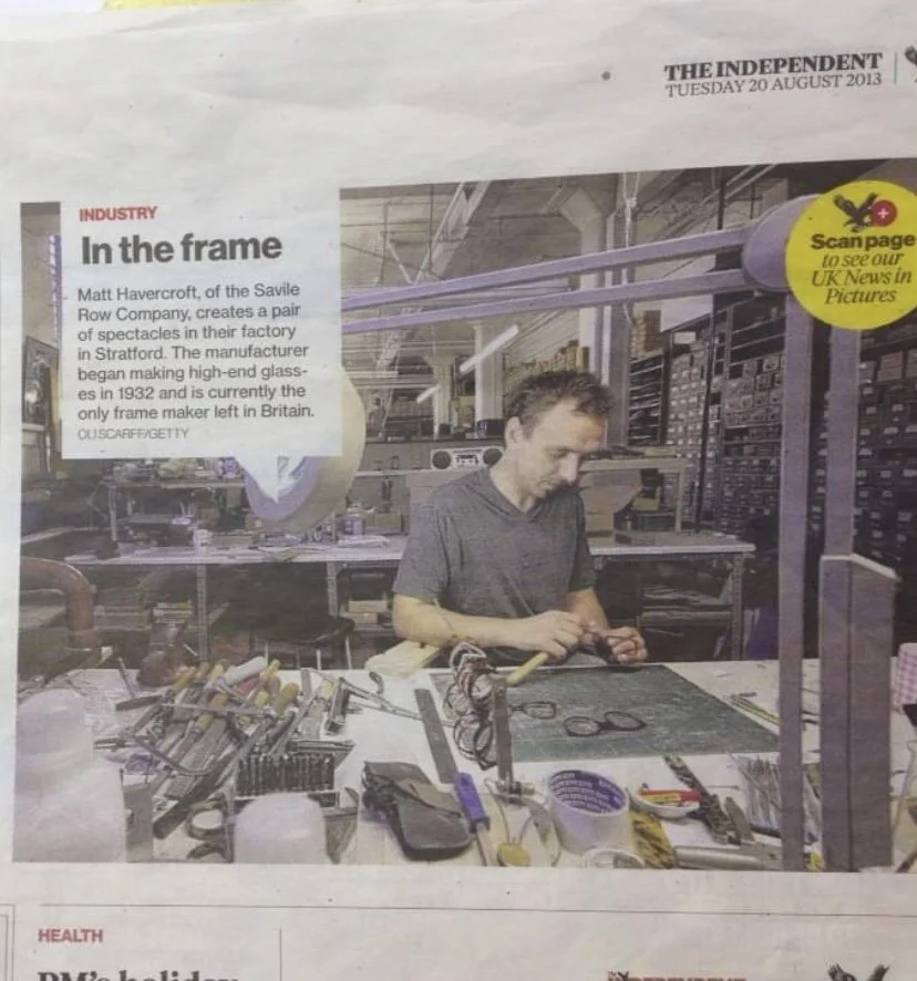 A man working in a factory creating high-end glasses at the Savile Row Company factory in Britain, surrounded by tools and equipment.