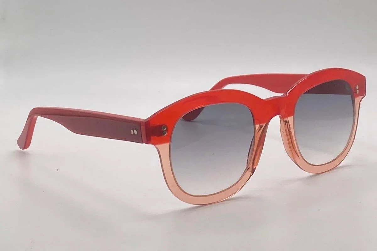 Red and pink sunglasses with gray lenses on a plain white surface.