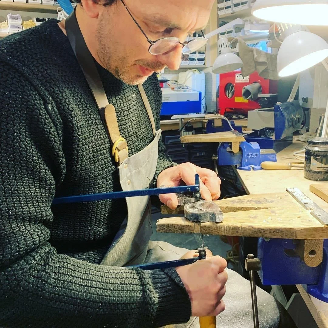A man working in a workshop, using a hand saw to cut a piece of wood secured in a vice.