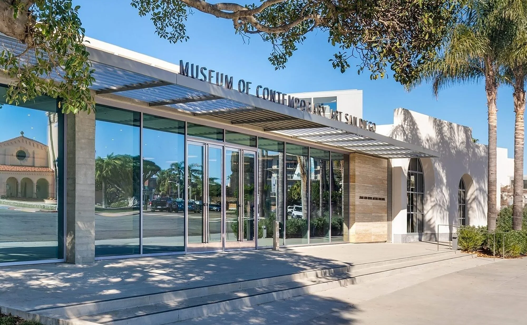 Exterior of the Museum of Contemporary Art San Diego, with glass doors, trees, and palm trees on a sunny day.
