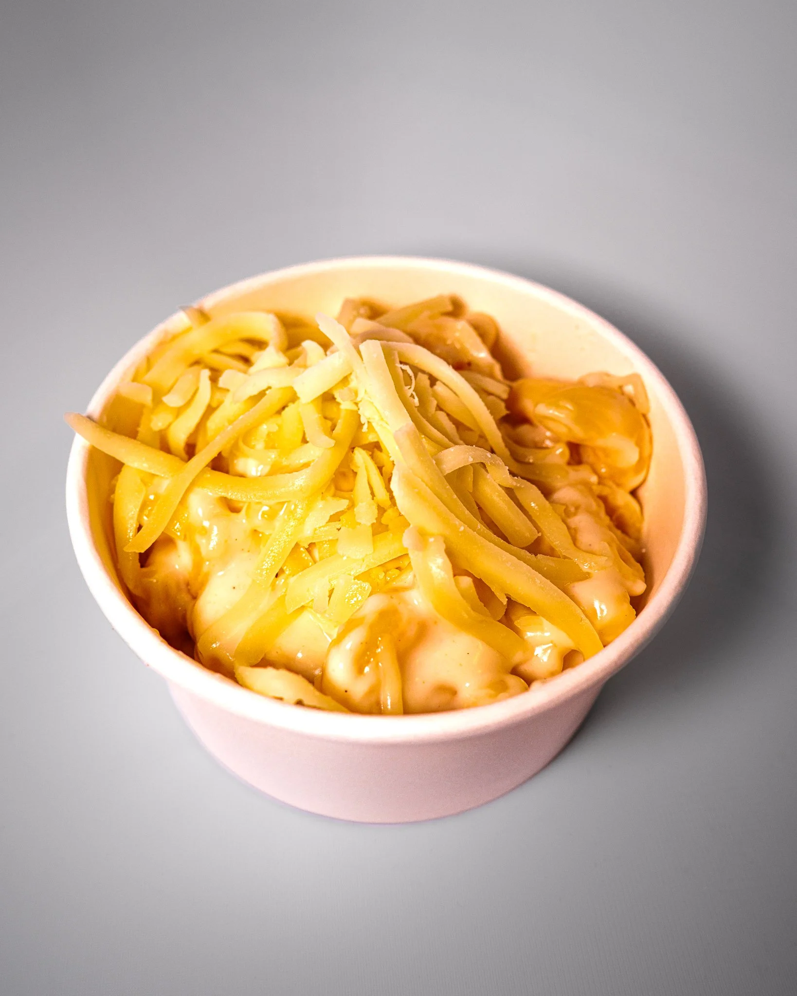 A pink bowl filled with macaroni and cheese topped with shredded cheese.