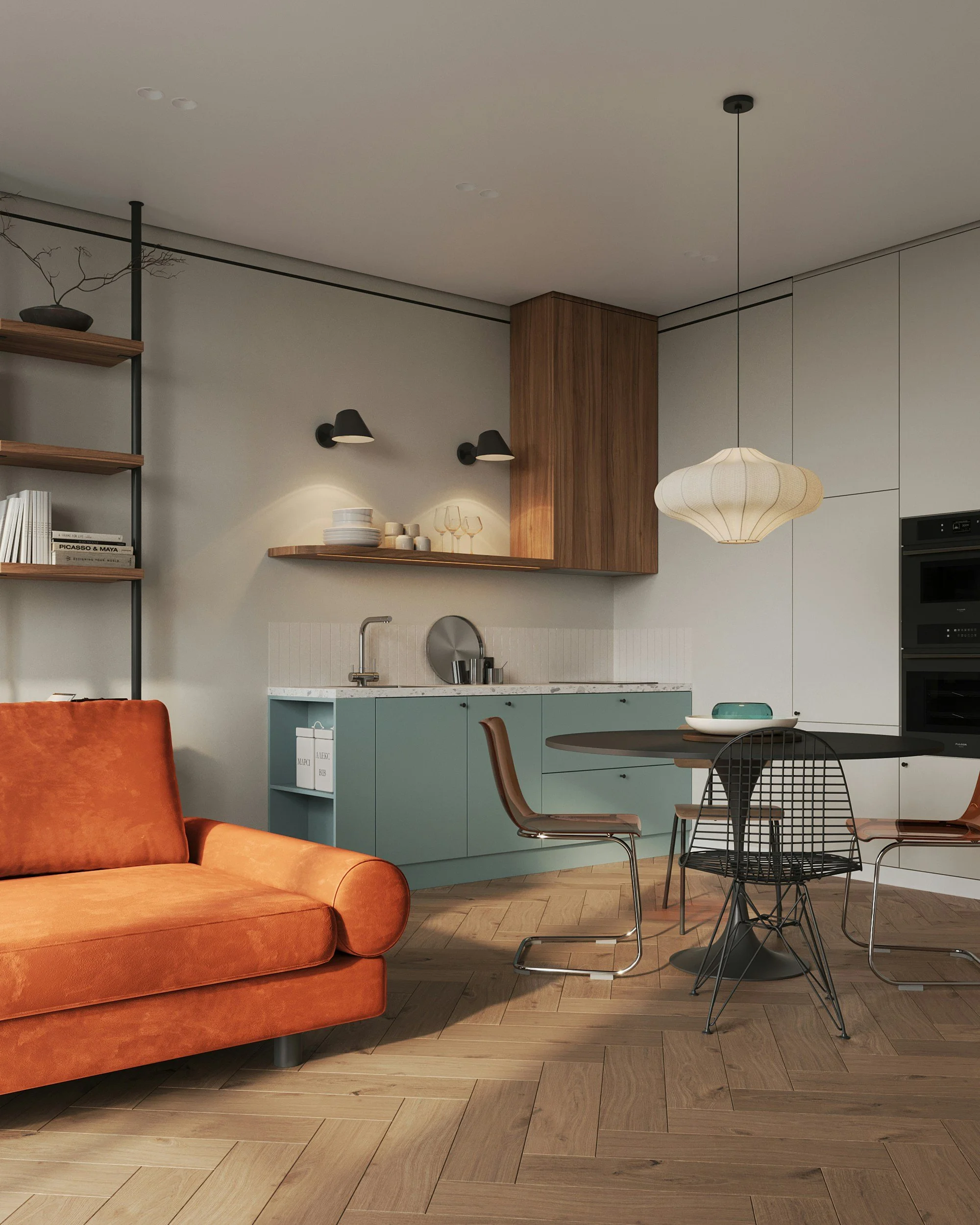 Interior view of a modern open-plan living area with a burnt orange sofa, a round black dining table, mixed chairs, a small kitchen with teal lower cabinets, wooden upper cabinets, a hanging pendant light, and shelves with books and decorative items.