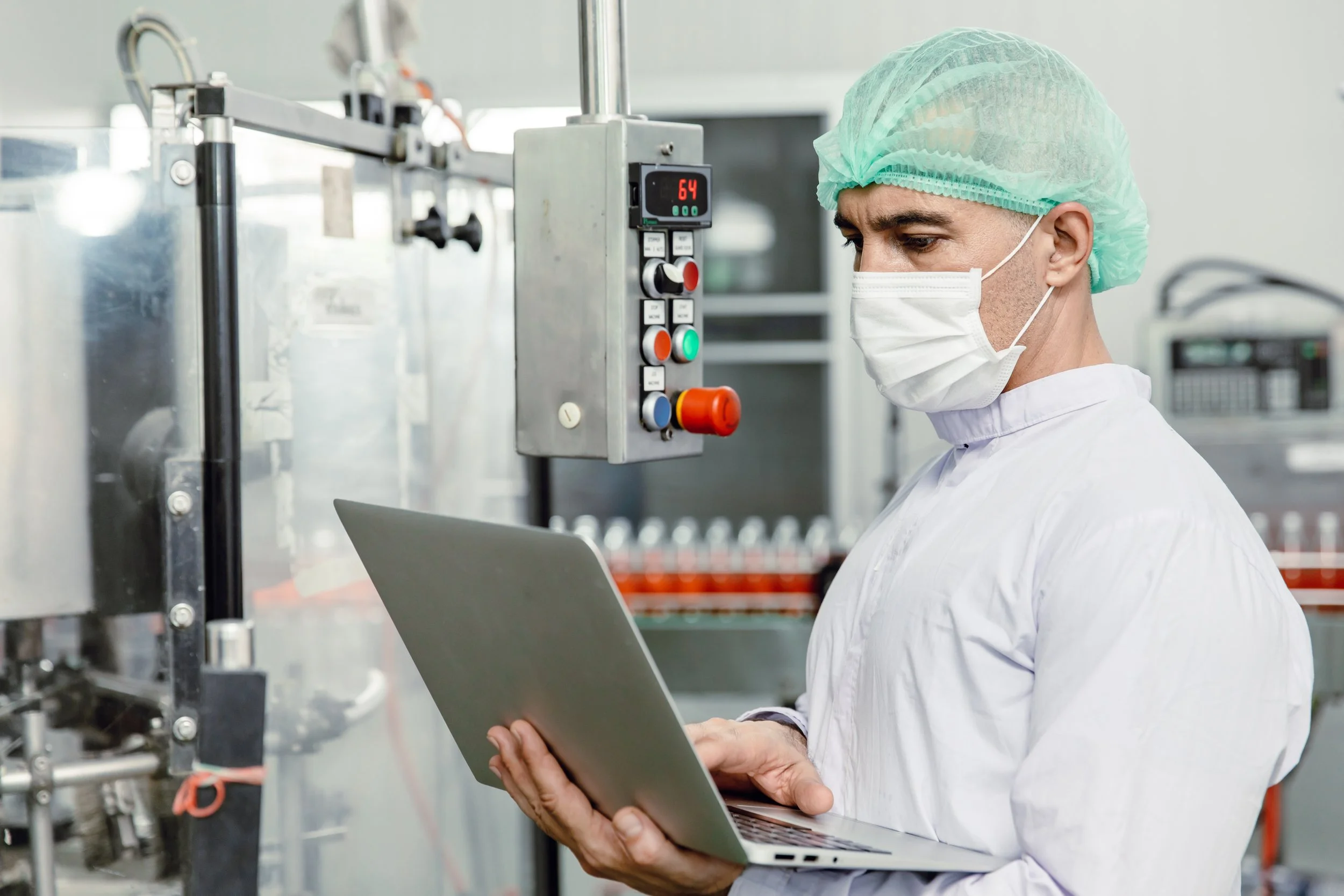 A worker in medical protective gear looks at a laptop in a science research setting.