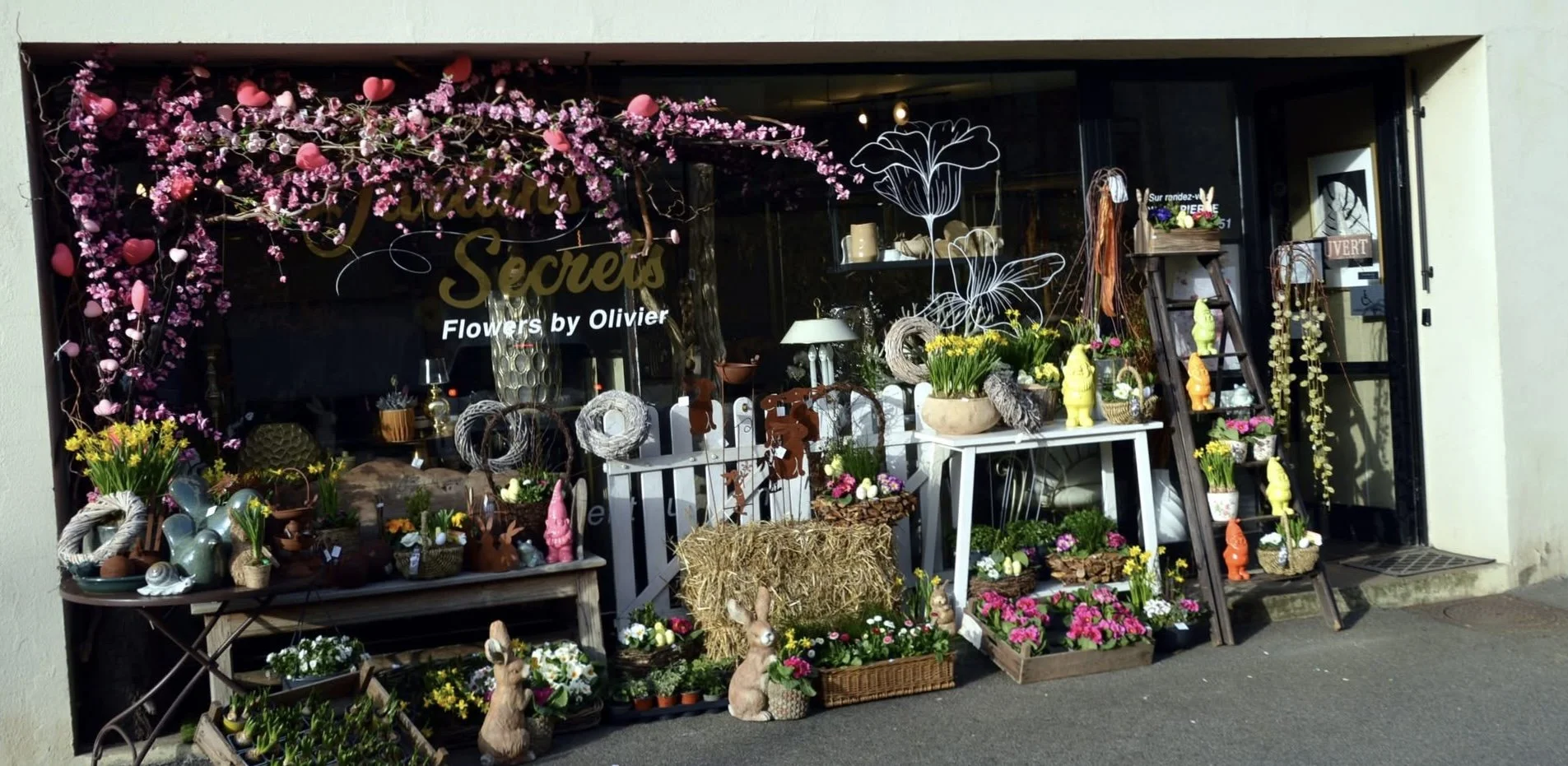 Vitrine de boutique de fleurs décorée avec des fleurs colorées, des figurines en forme de lapins et des objets décoratifs, en plein air.