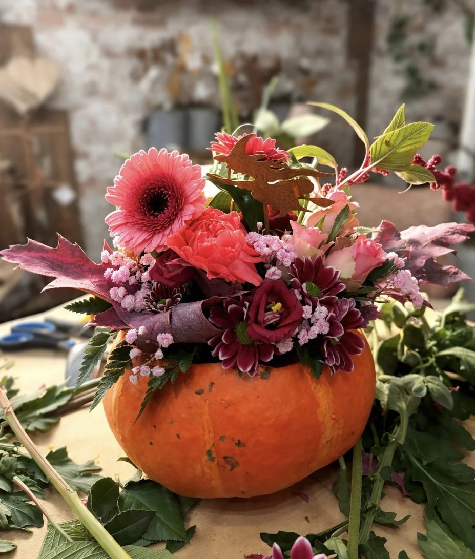 Un arrangement floral dans une citrouille orange avec des fleurs roses, rouges et violettes dans un environnement intérieur fleuriste à Florange