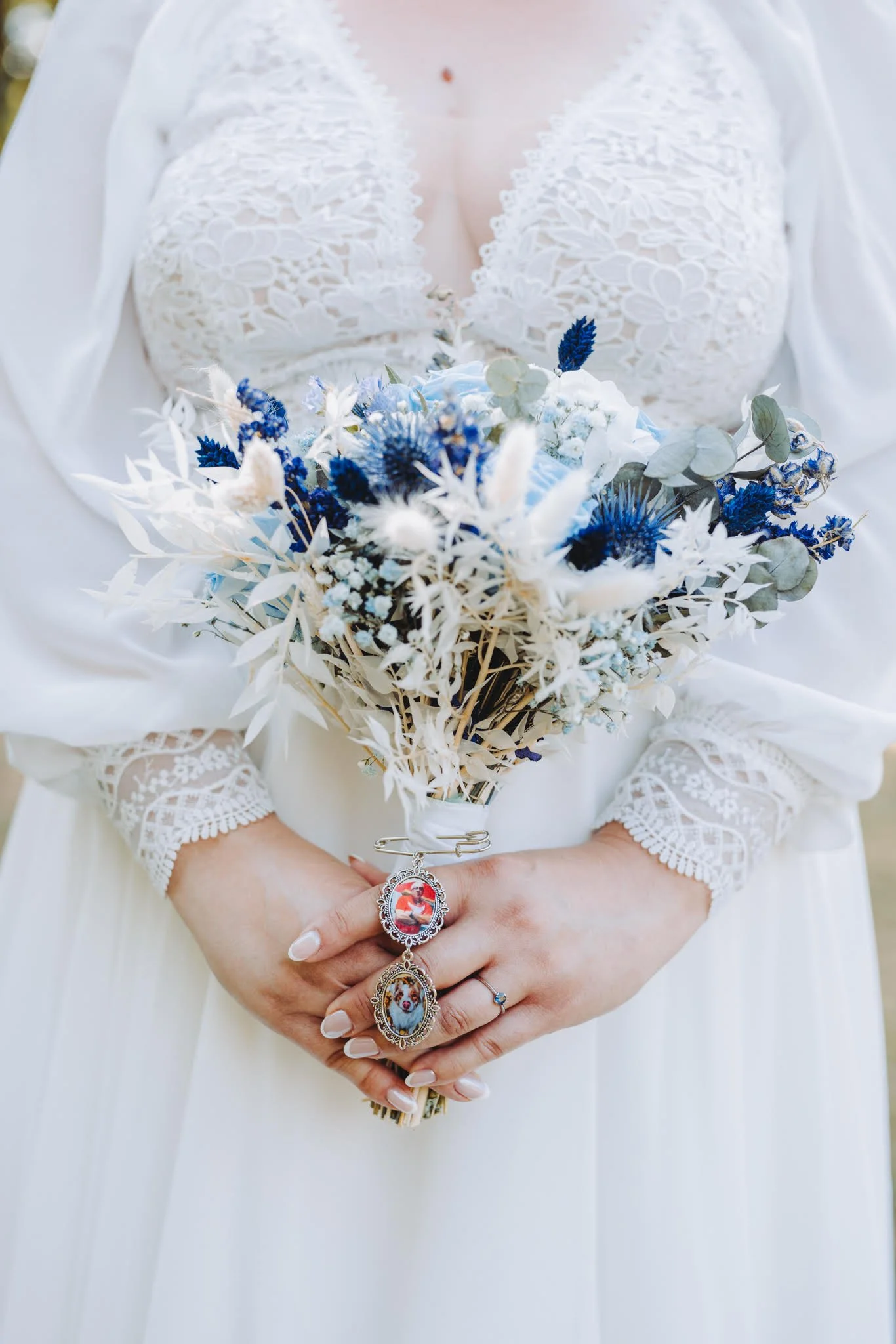Femme en robe de mariée blanche tenant un bouquet de fleurs blanches et bleues, portant deux broches avec des images de chiens.