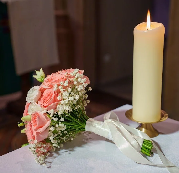 Un bouquet de fleurs roses et blanches, avec une bougie allumée à côté, sur une table.