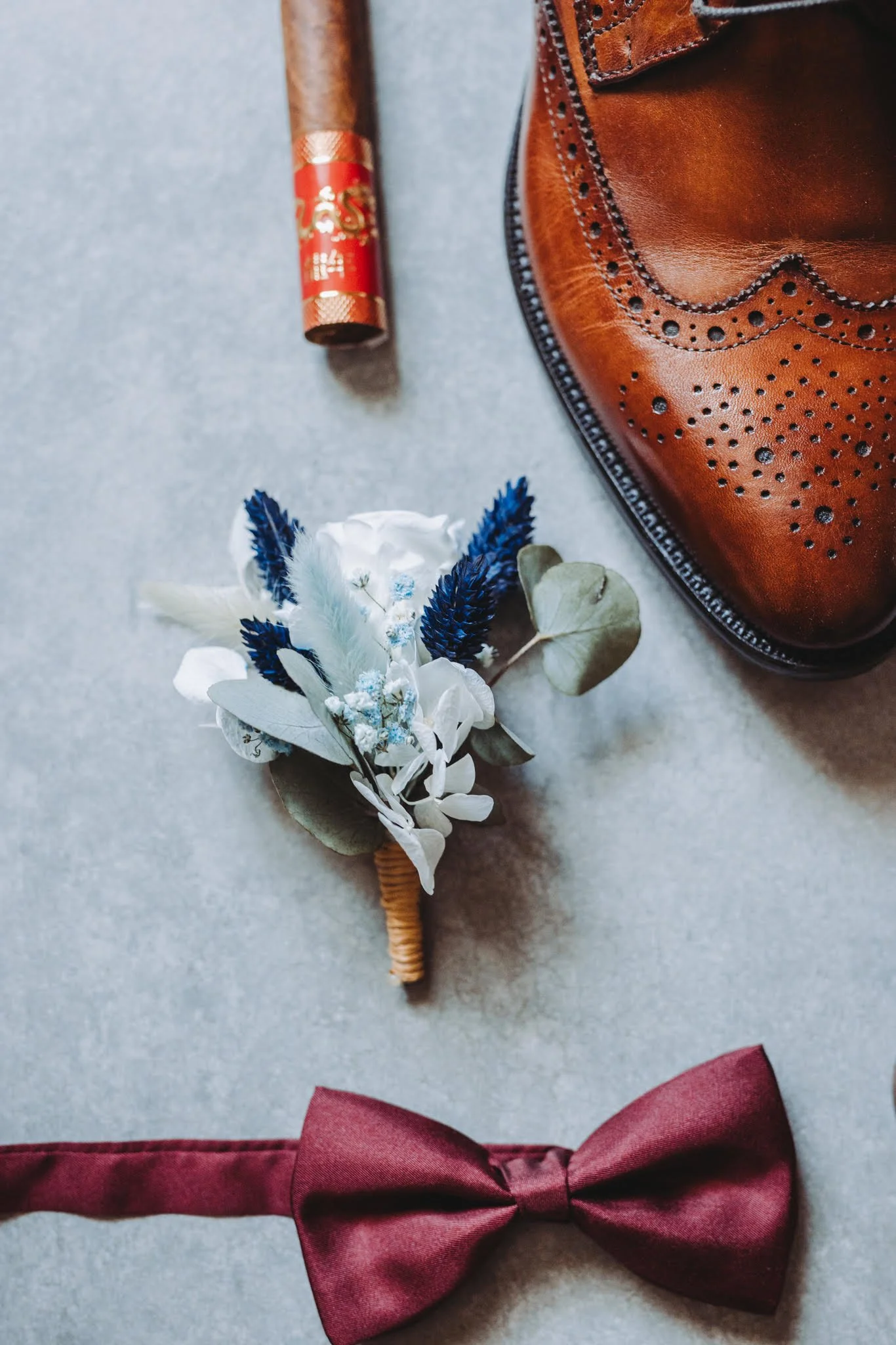 Accessoires masculins et éléments de fête: cigare, chaussure en cuir, bouton de mariage, boutonnière florale, nœud papillon rouge.