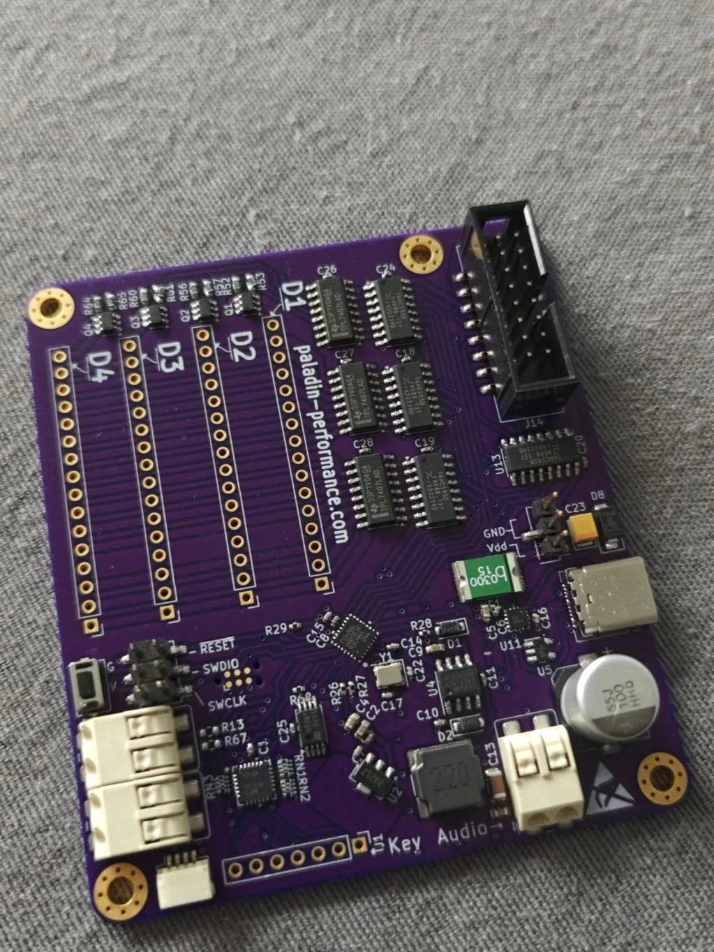 Purple electronic circuit board with various chips, connectors, and components on a gray fabric surface.
