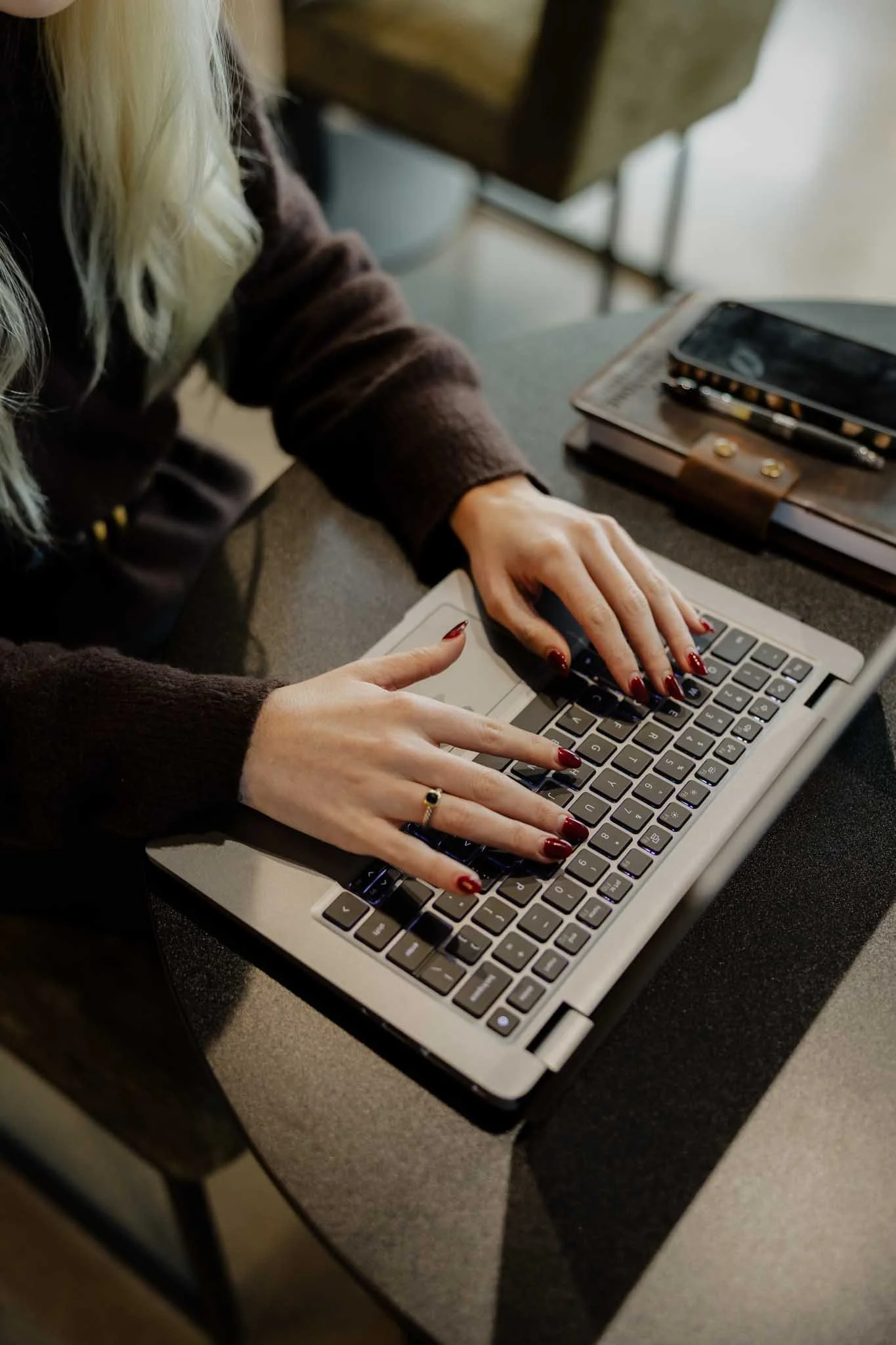 A person typing on a laptop keyboard placed on a desk with a notebook, smartphone, and pen.