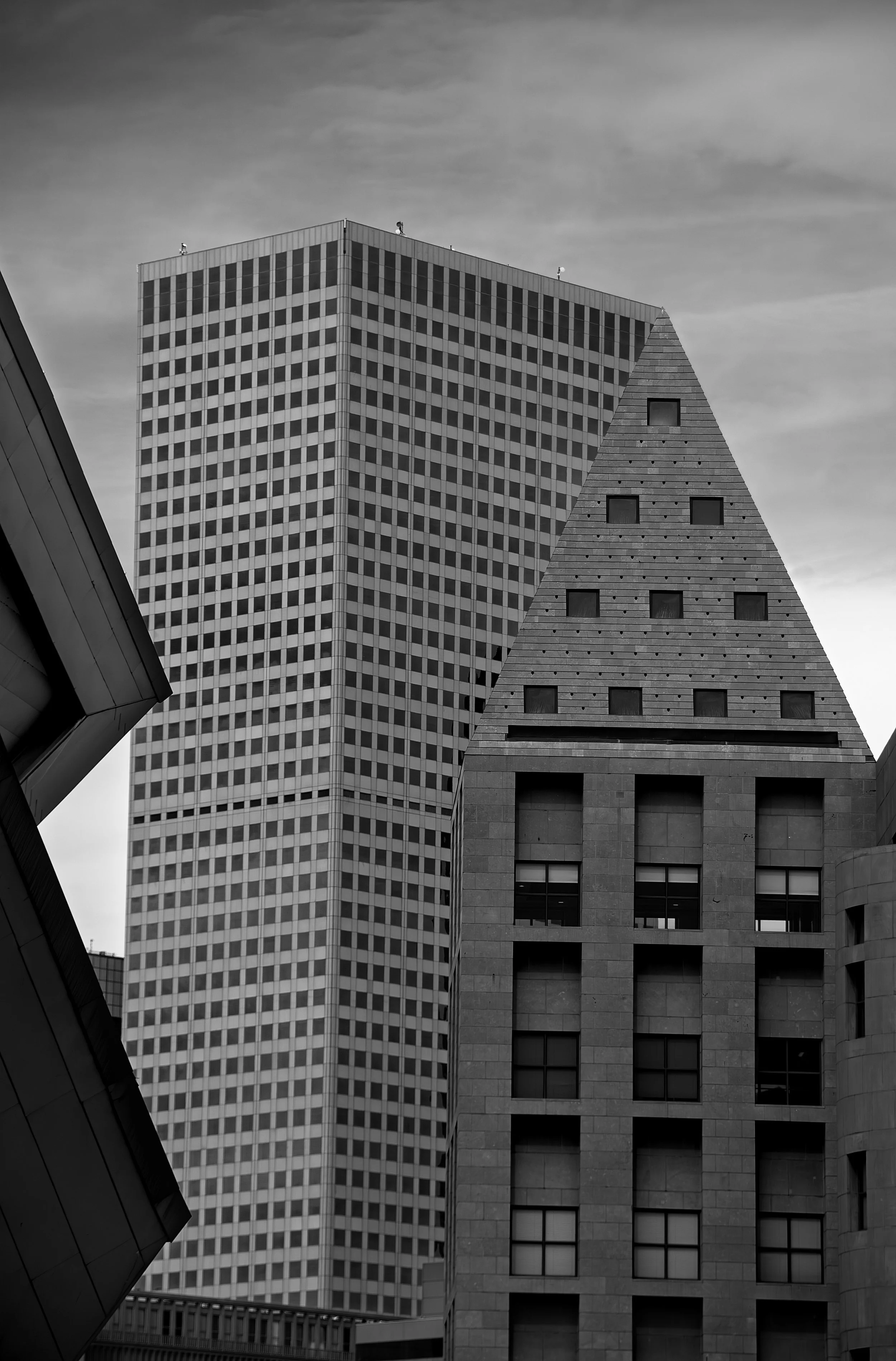 Black-and-white photo of three buildings with varying architectural styles, with a cloudy sky in the background.