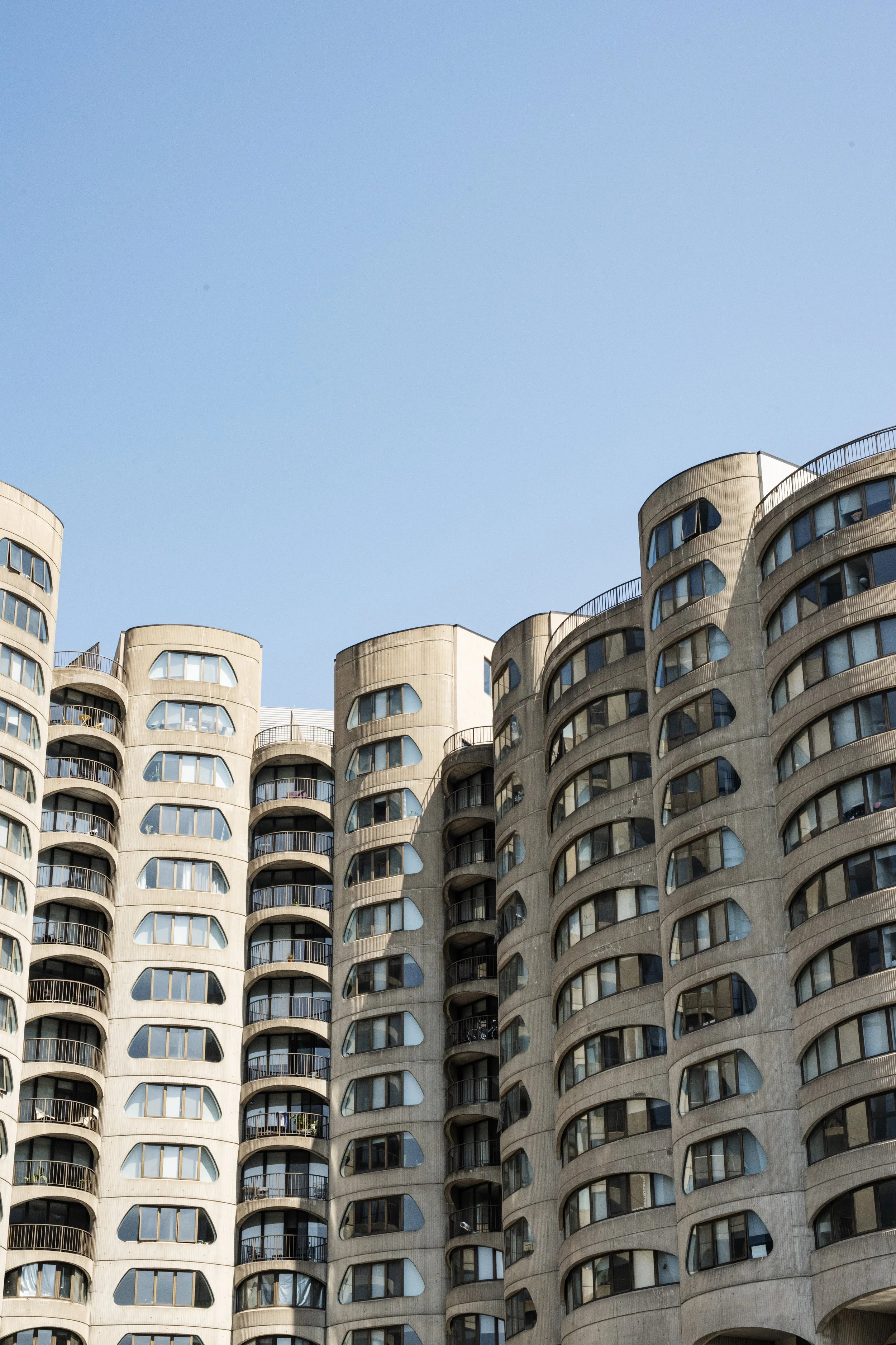 Close-up view of a modern residential building with rounded balconies and large windows, against a clear blue sky.