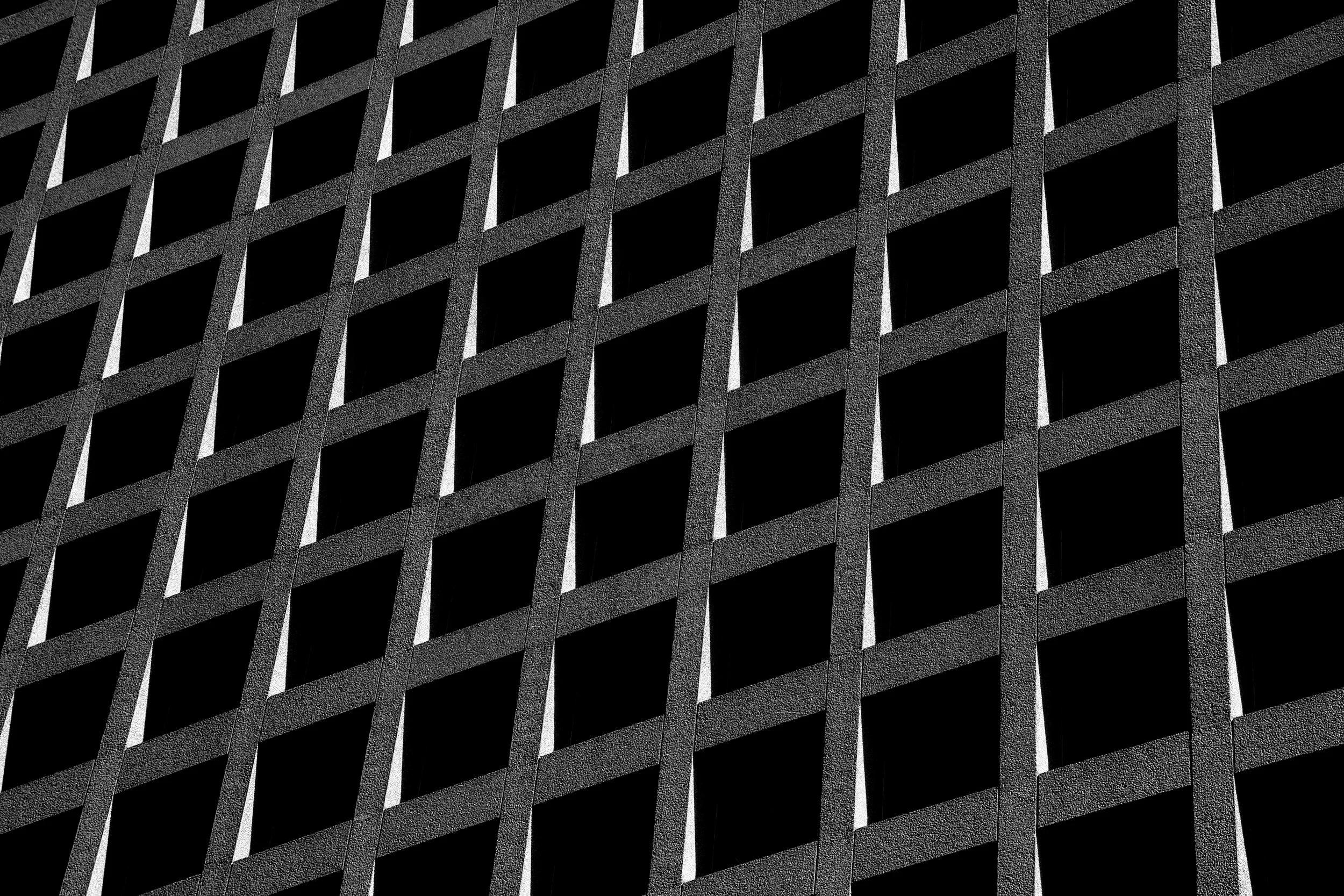 Close-up view of a modern building facade with a repeating pattern of window openings and concrete frames, creating a geometric grid.