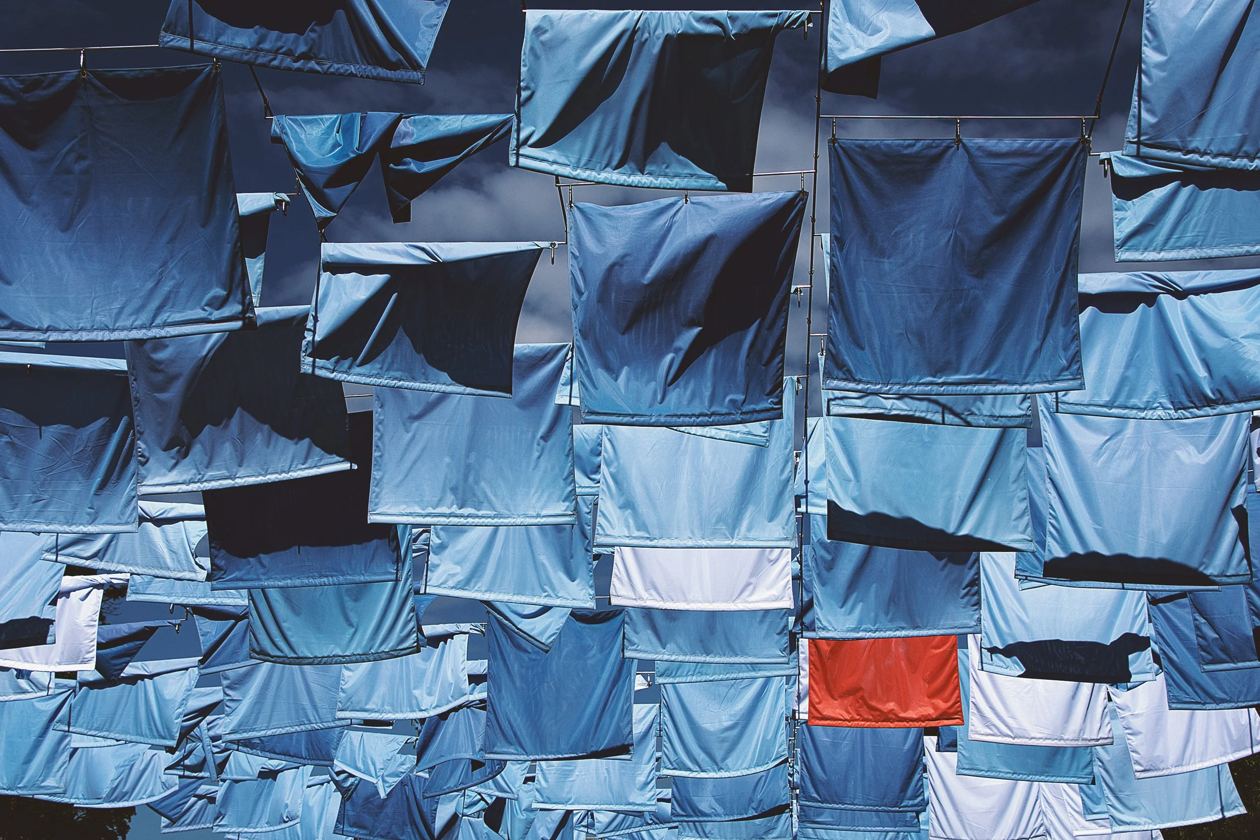 A large outdoor art installation of laundry hanging on lines, with a cloudy sky in the background.