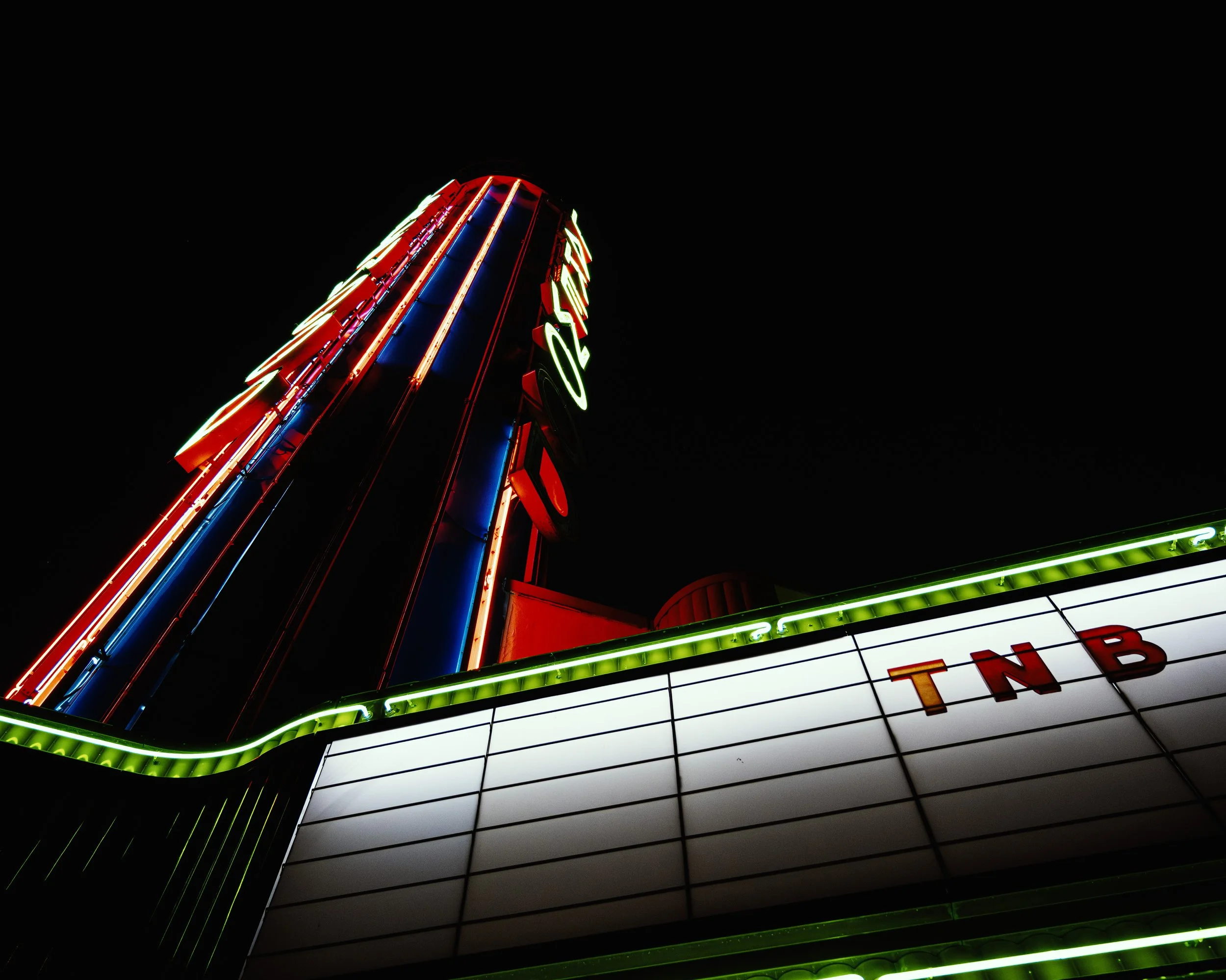 Neon-lit signs of a building at night with red, blue, green, and white lights against a dark sky.