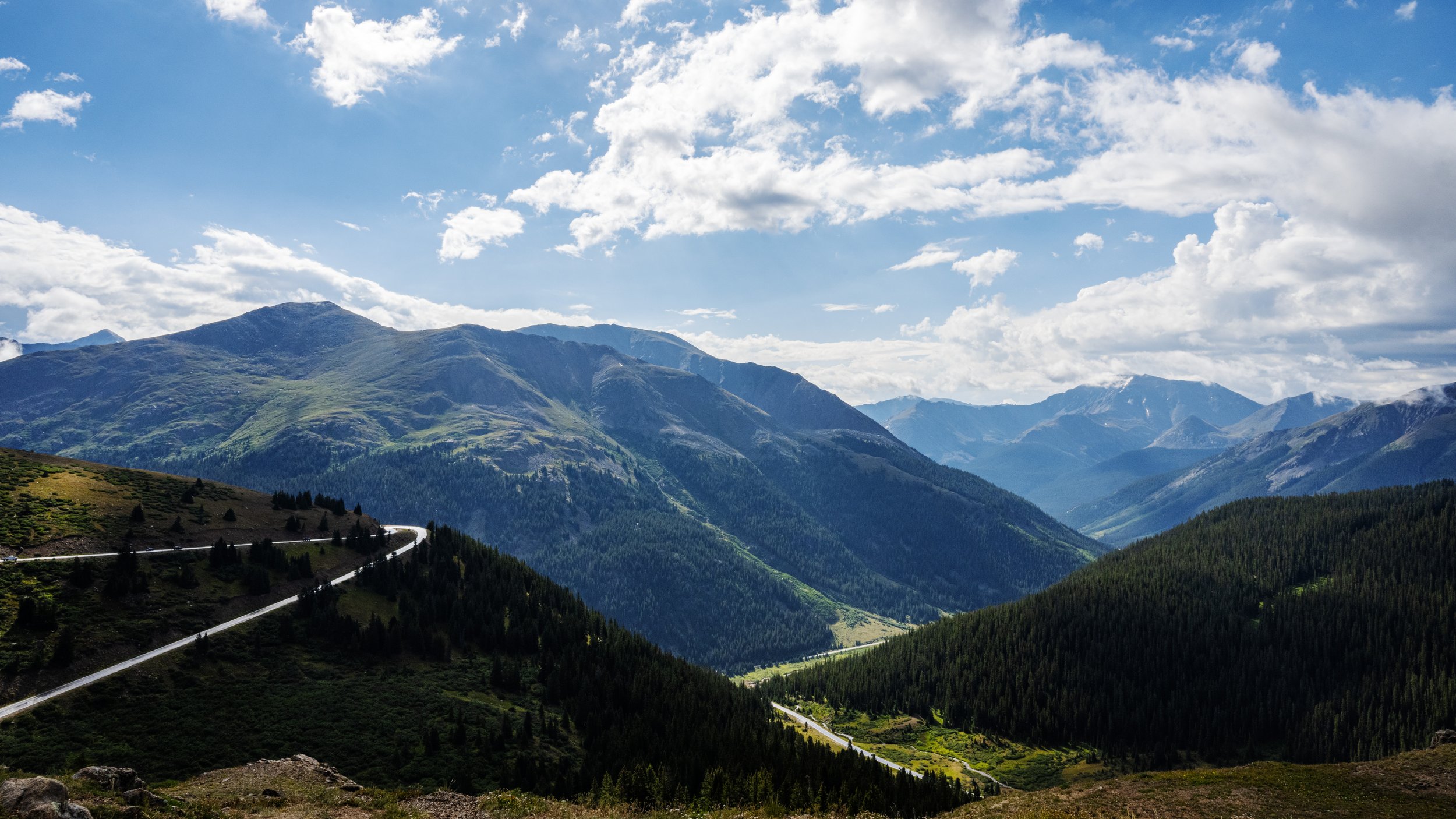 Scenic mountain landscape with green hills, winding road, and partly cloudy sky.