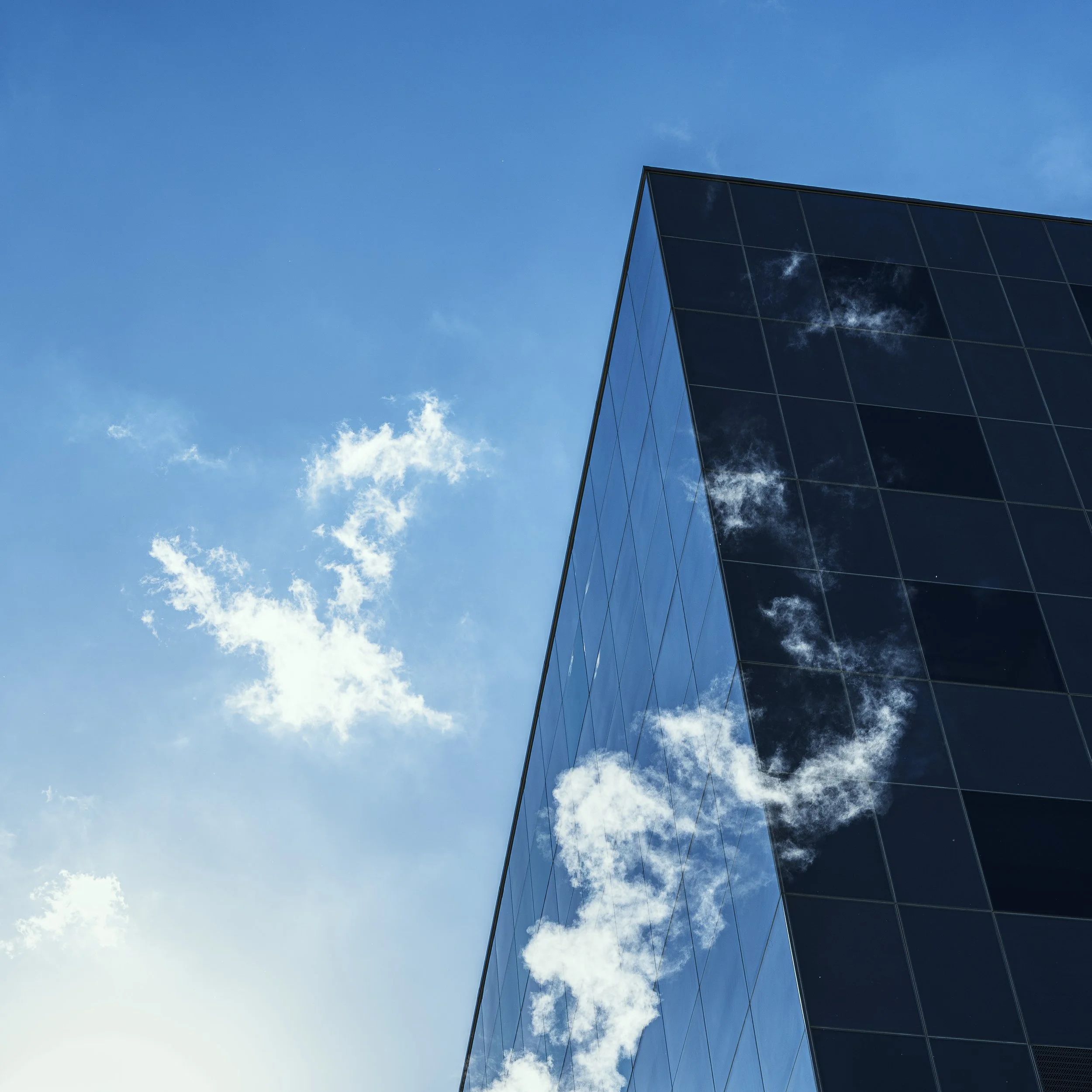 Close-up of a modern glass building reflecting the blue sky and scattered white clouds.