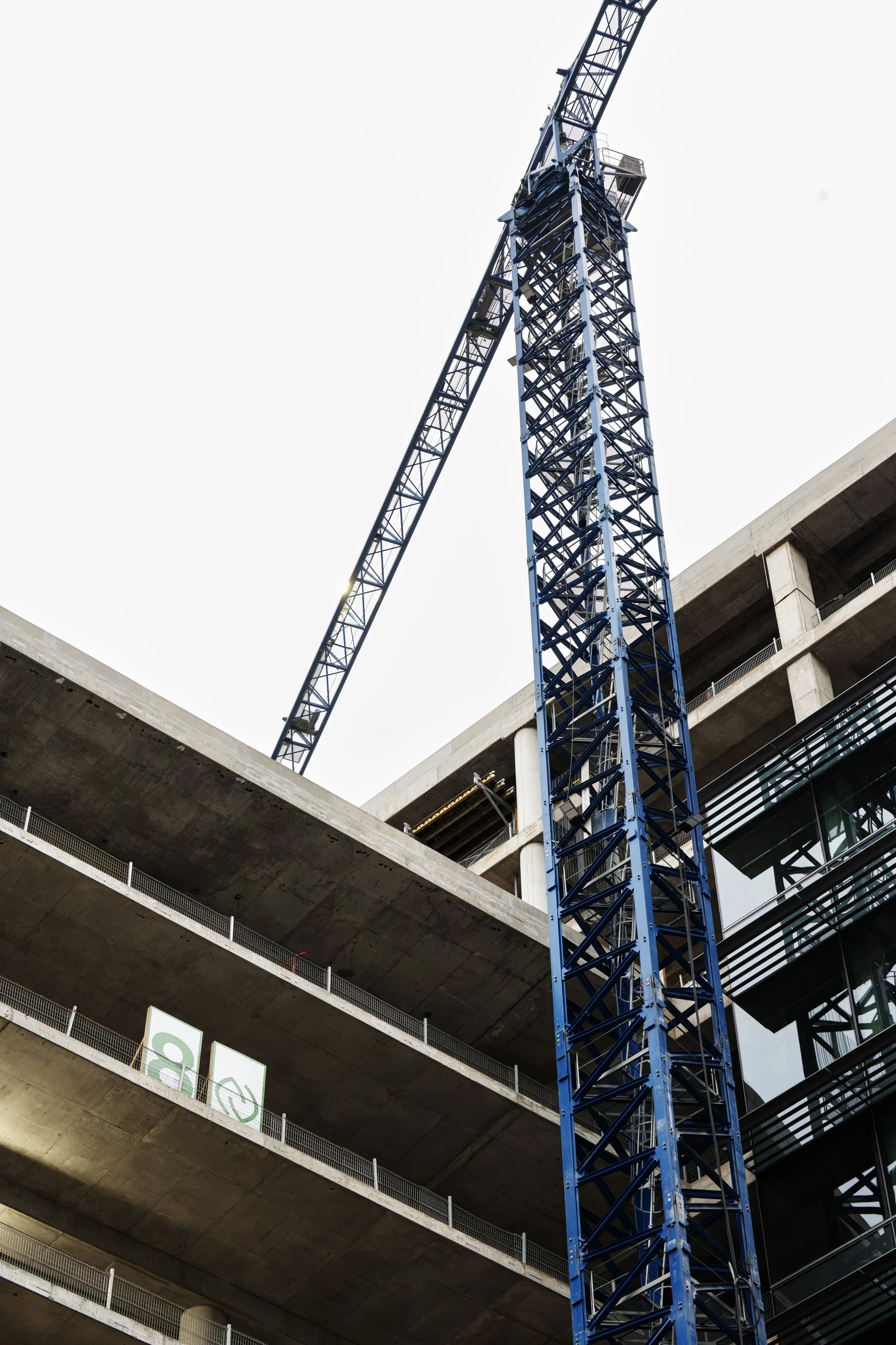 A construction site with a tall blue crane next to a multi-story concrete building under construction.