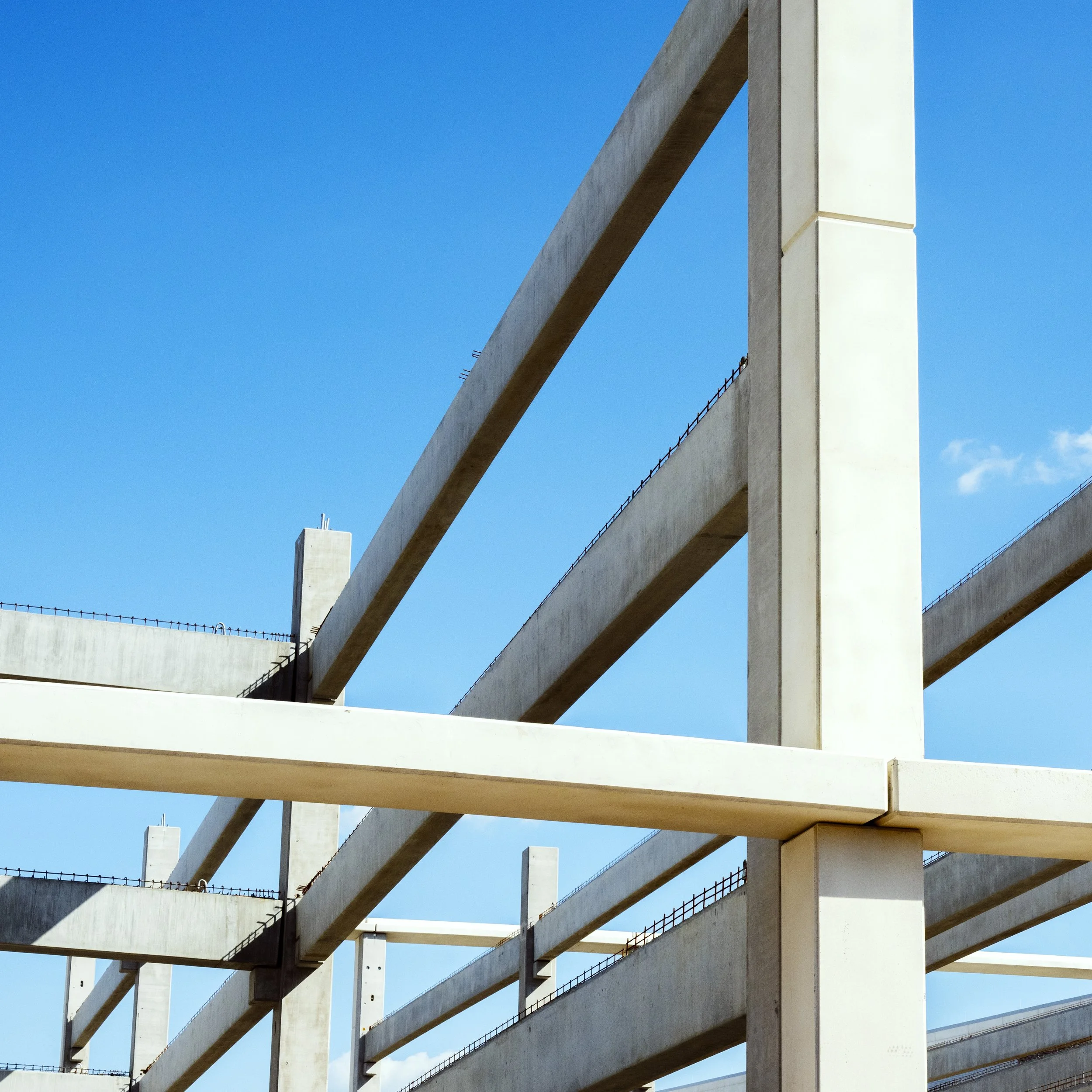 Close-up view of a modern building under construction with concrete beams and a bright blue sky in the background.
