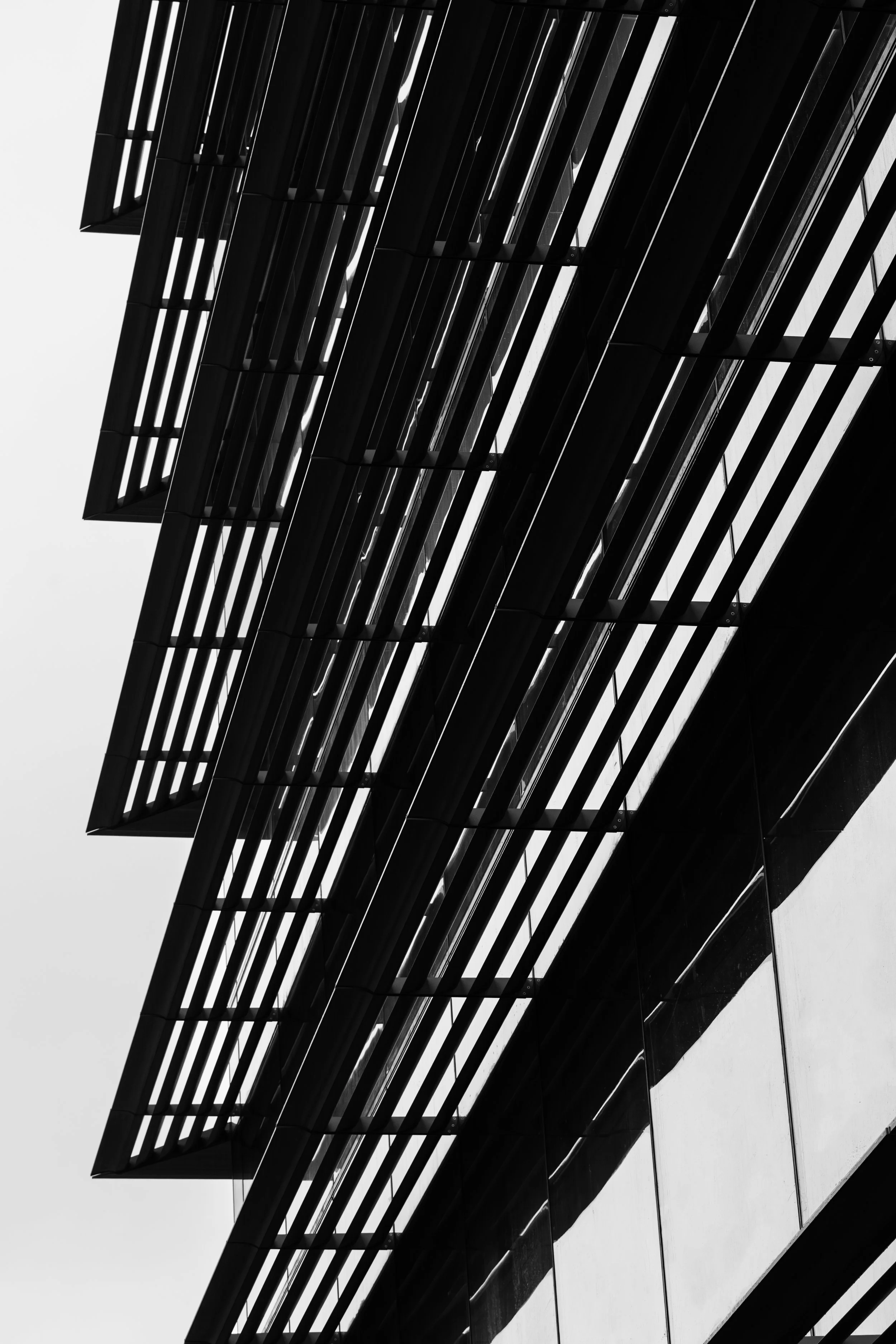 Close-up shot of a modern building facade with horizontal and vertical black louvered panels, creating a geometric pattern on the glass exterior.
