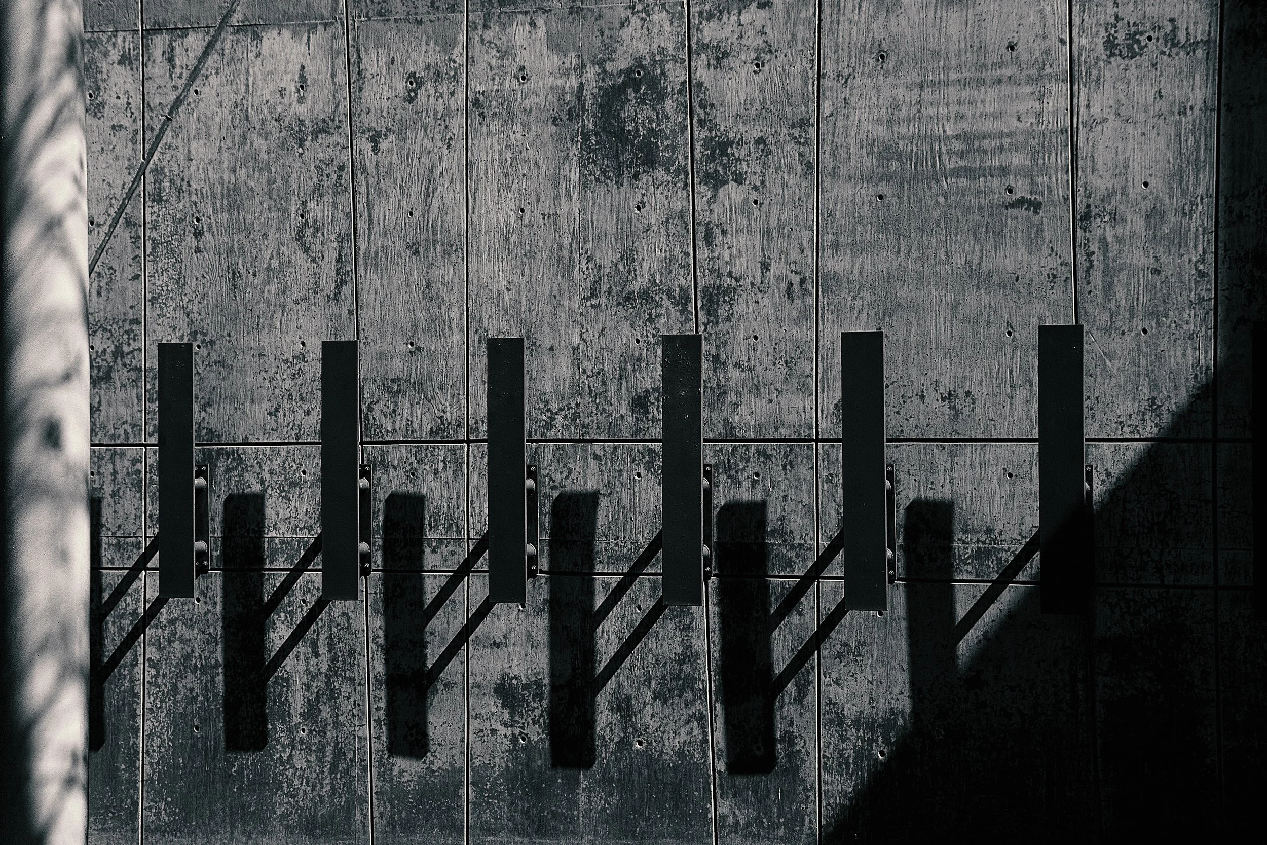A close-up view of a concrete wall with black metal vertical bars casting shadows on it.