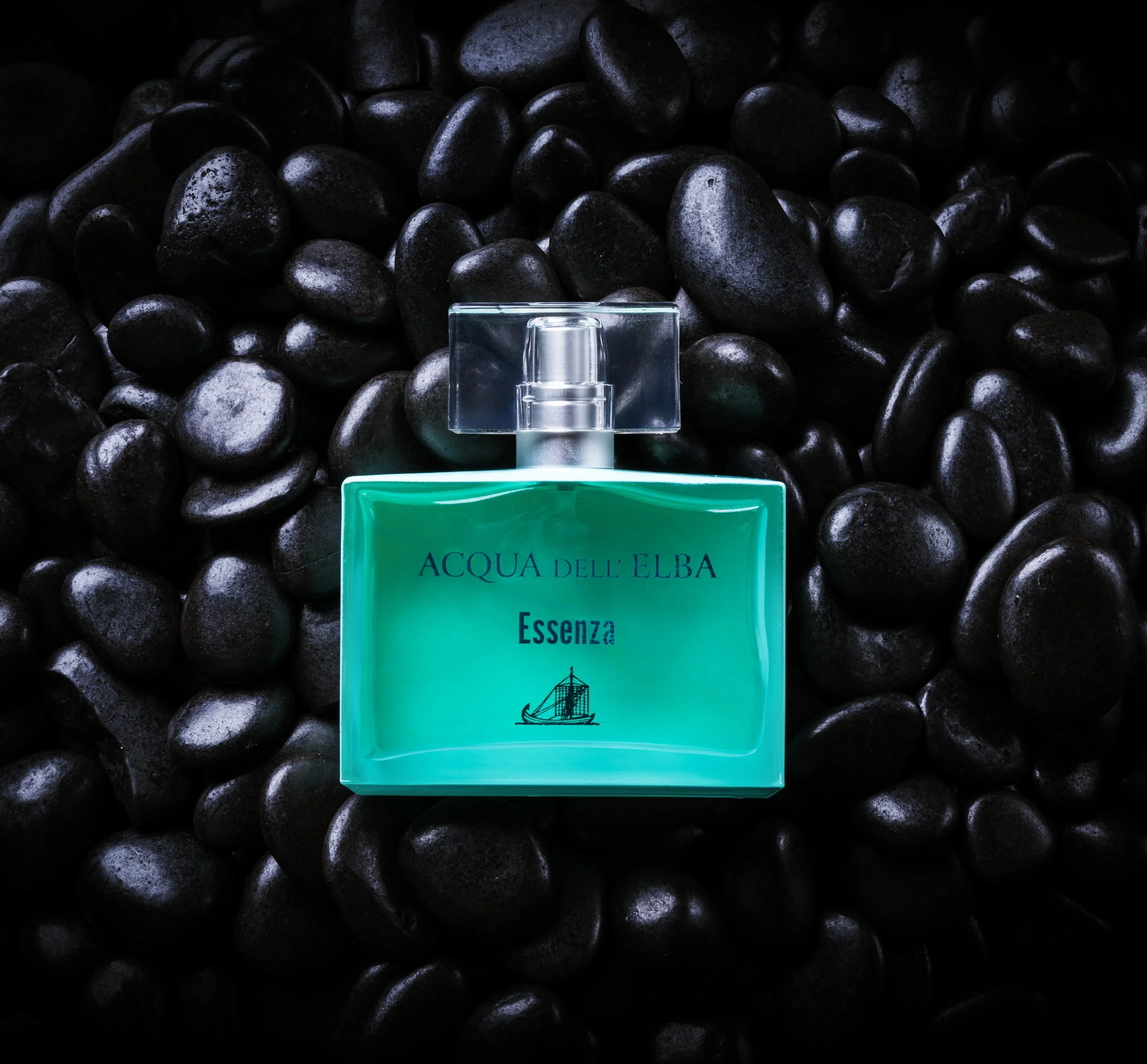 A bottle of Acqua dell'Elba Essenza perfume against a background of black stones.