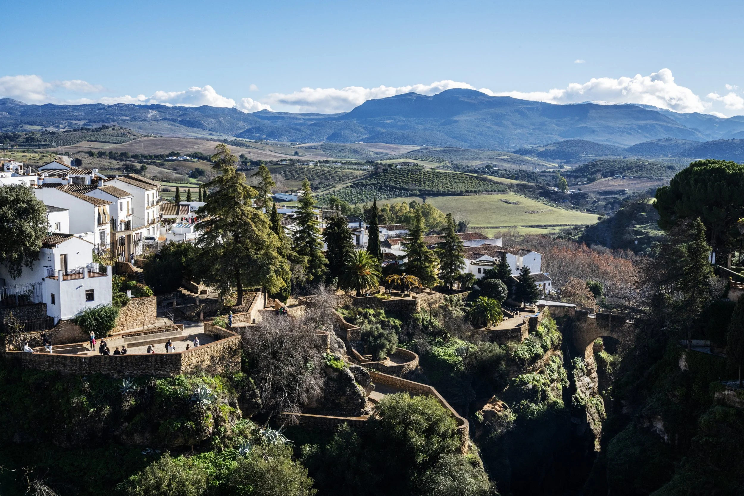 A scenic view of a mountain landscape with rolling hills, partly cloudy sky, and traditional white houses with tiled roofs in the foreground.